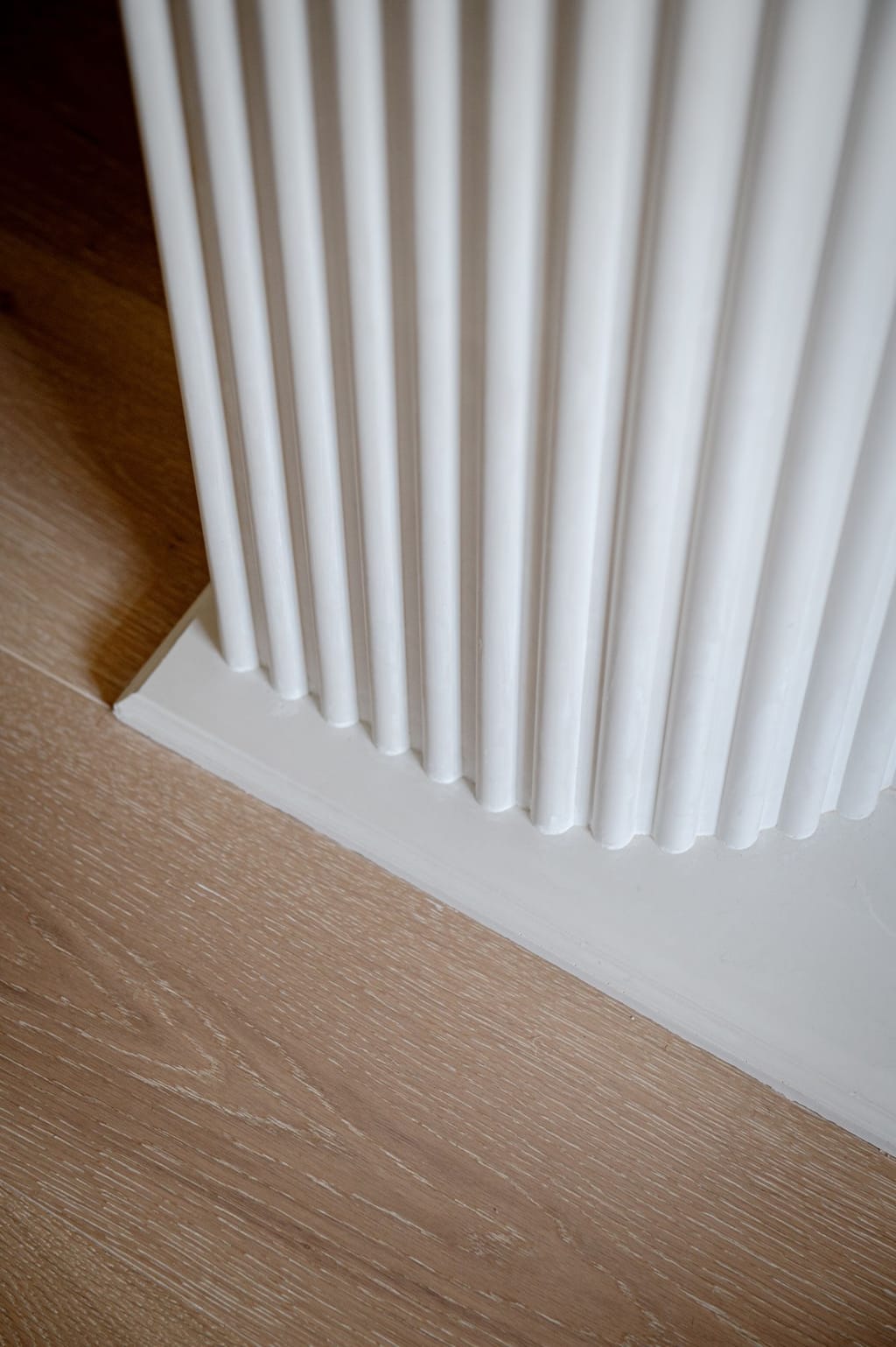 Close view of the fluted plaster fireplace base meeting a wide-plank oak floor