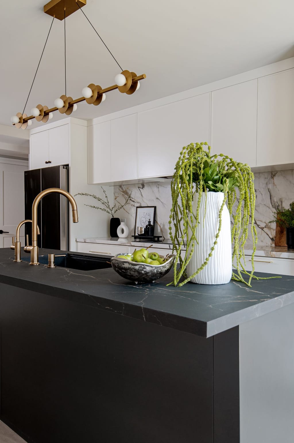 The black island with a brass faucet and filtered water tap, under a brass and white globe linear chandelier