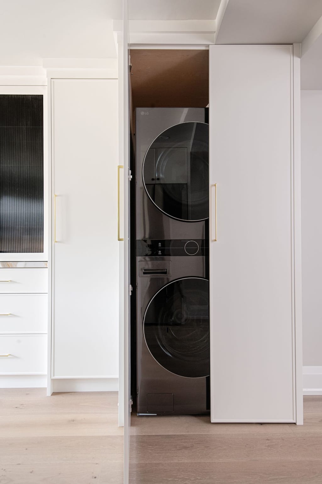 A tall white cabinet with its doors open on a stacked washer and dryer, set into the kitchen run