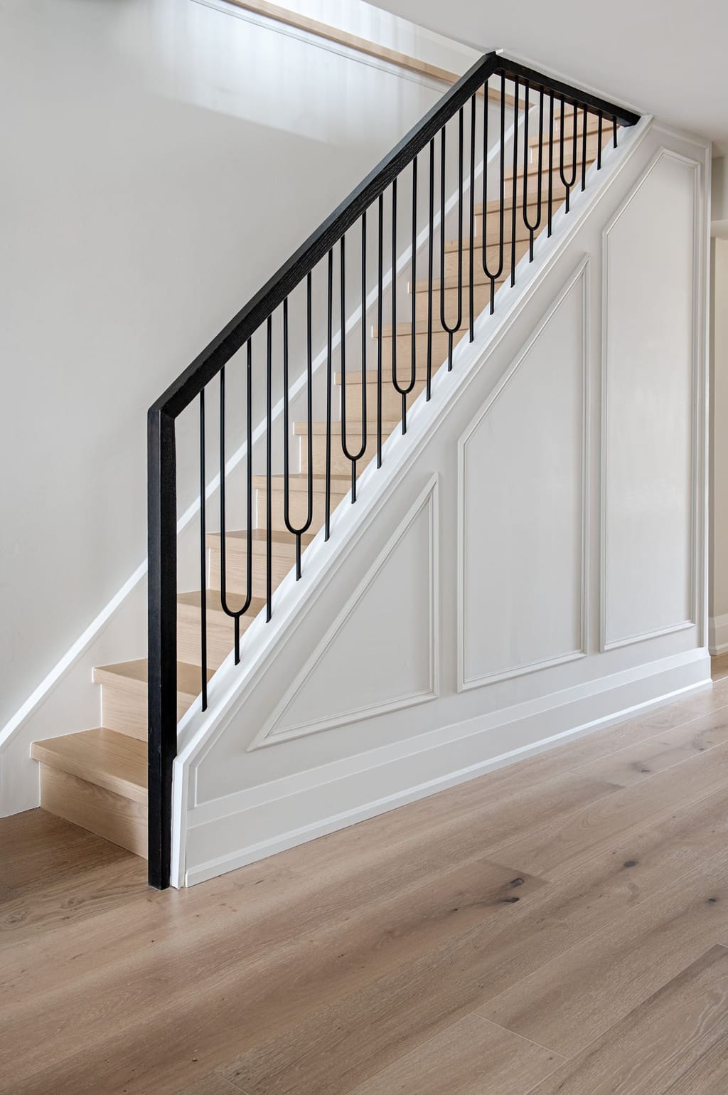 A steep stair with refinished oak treads, black looped balusters and a new white panelled wall under the stringer