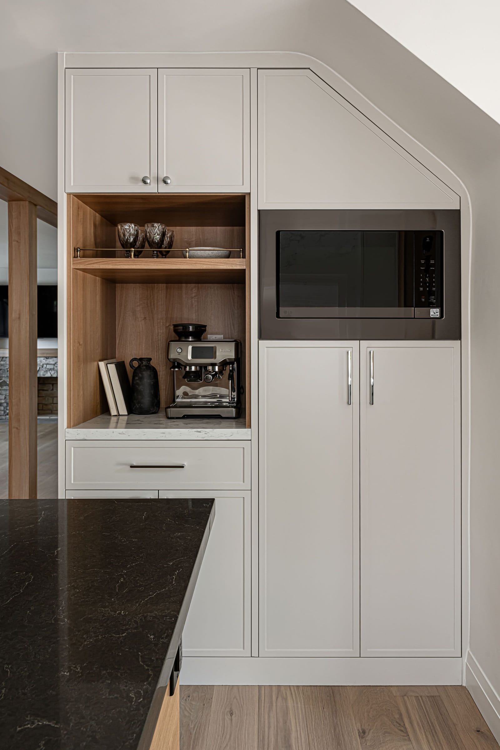 A tall cabinet wall with an oak-lined coffee niche, an espresso machine, a built-in microwave and an angled top that fits the ceiling