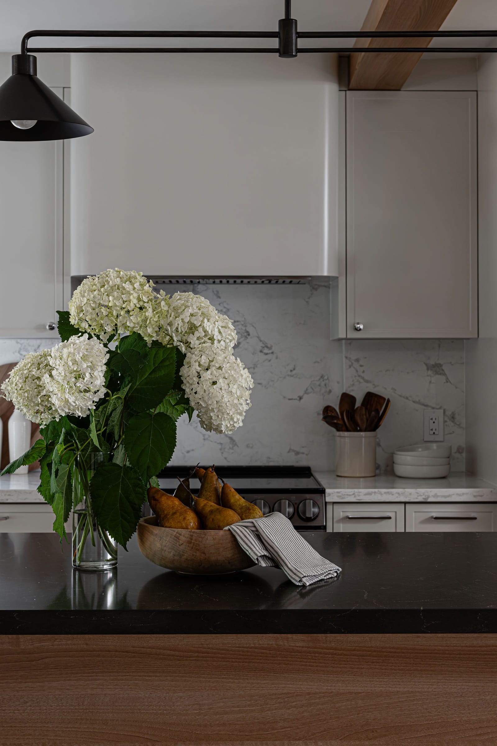 A plaster range hood with rounded corners between cream cabinets, over a quartz backsplash with grey veining
