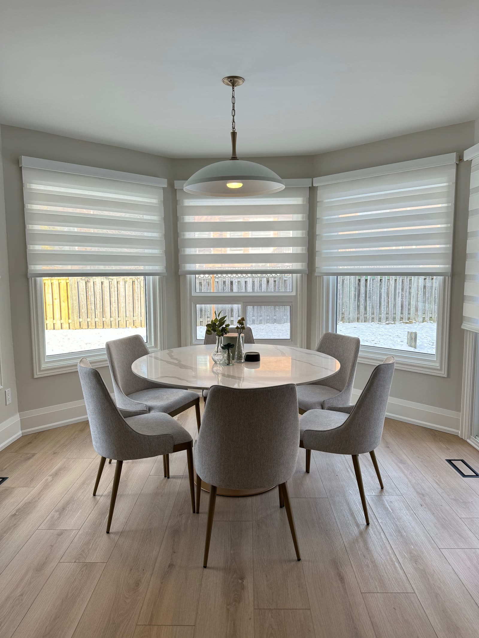 A breakfast nook in a bay window with a round stone table and grey chairs