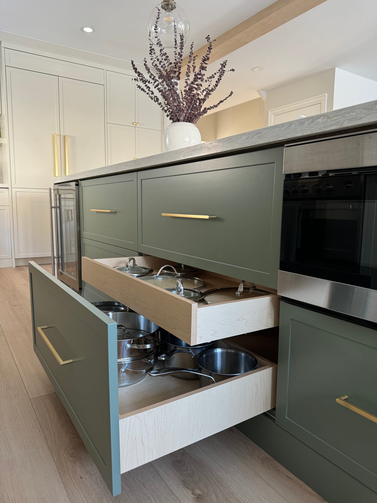 Deep pot drawers pulled out of the sage-green island beside a built-in oven