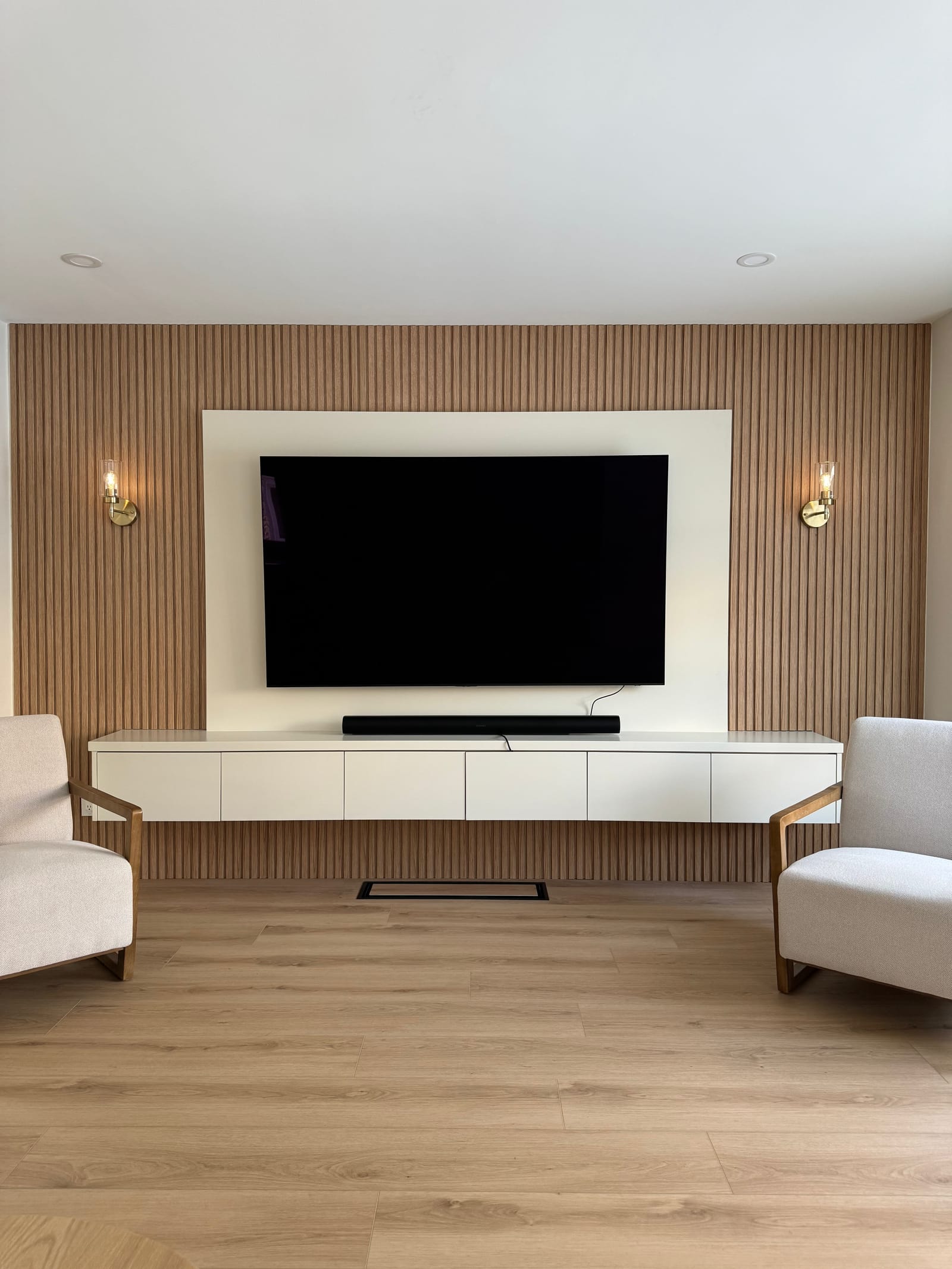 A media wall of oak slats with a white panel, a floating white cabinet and brass sconces