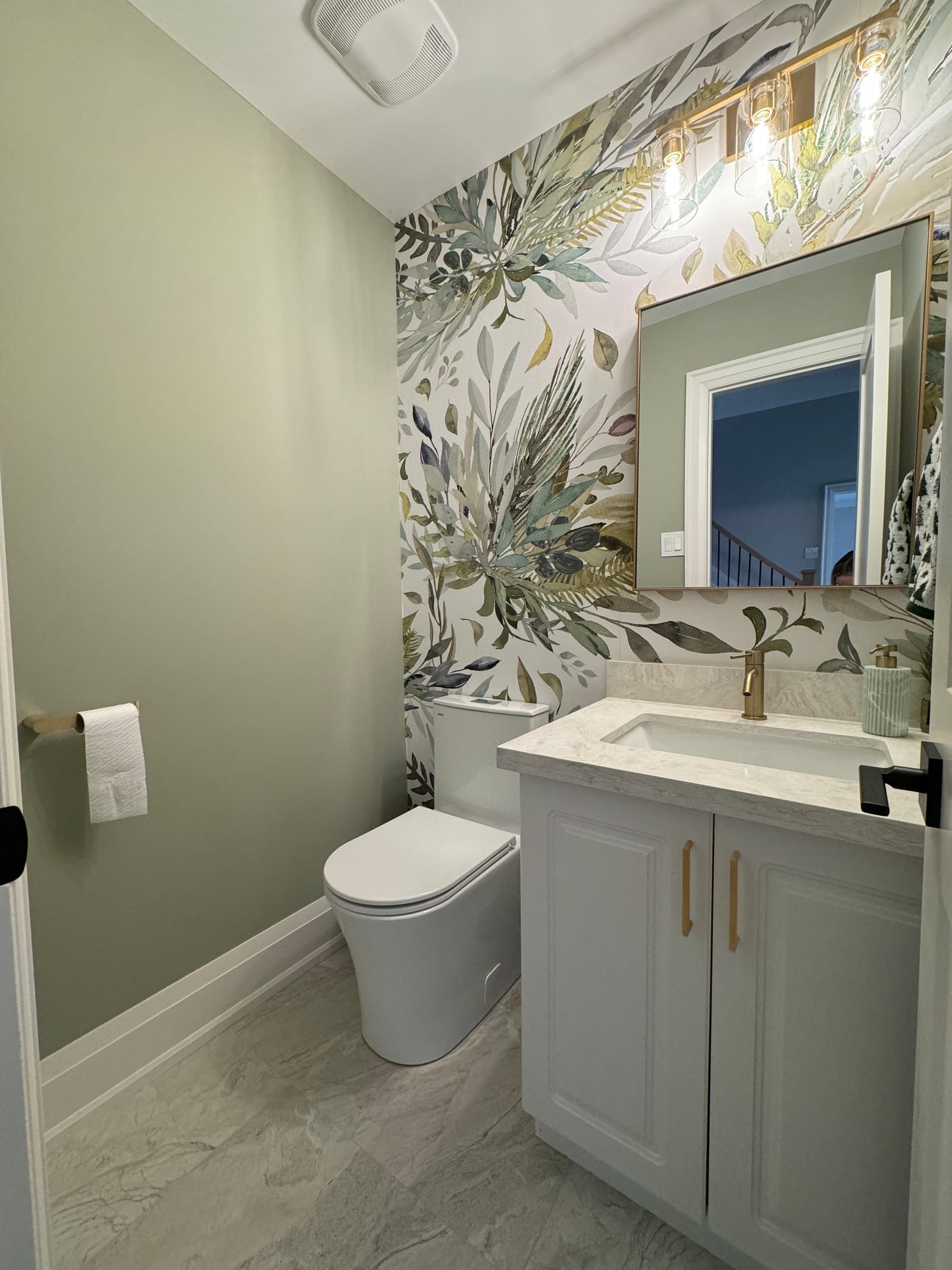 A powder room with a botanical wallpaper wall, sage paint and a grey vanity