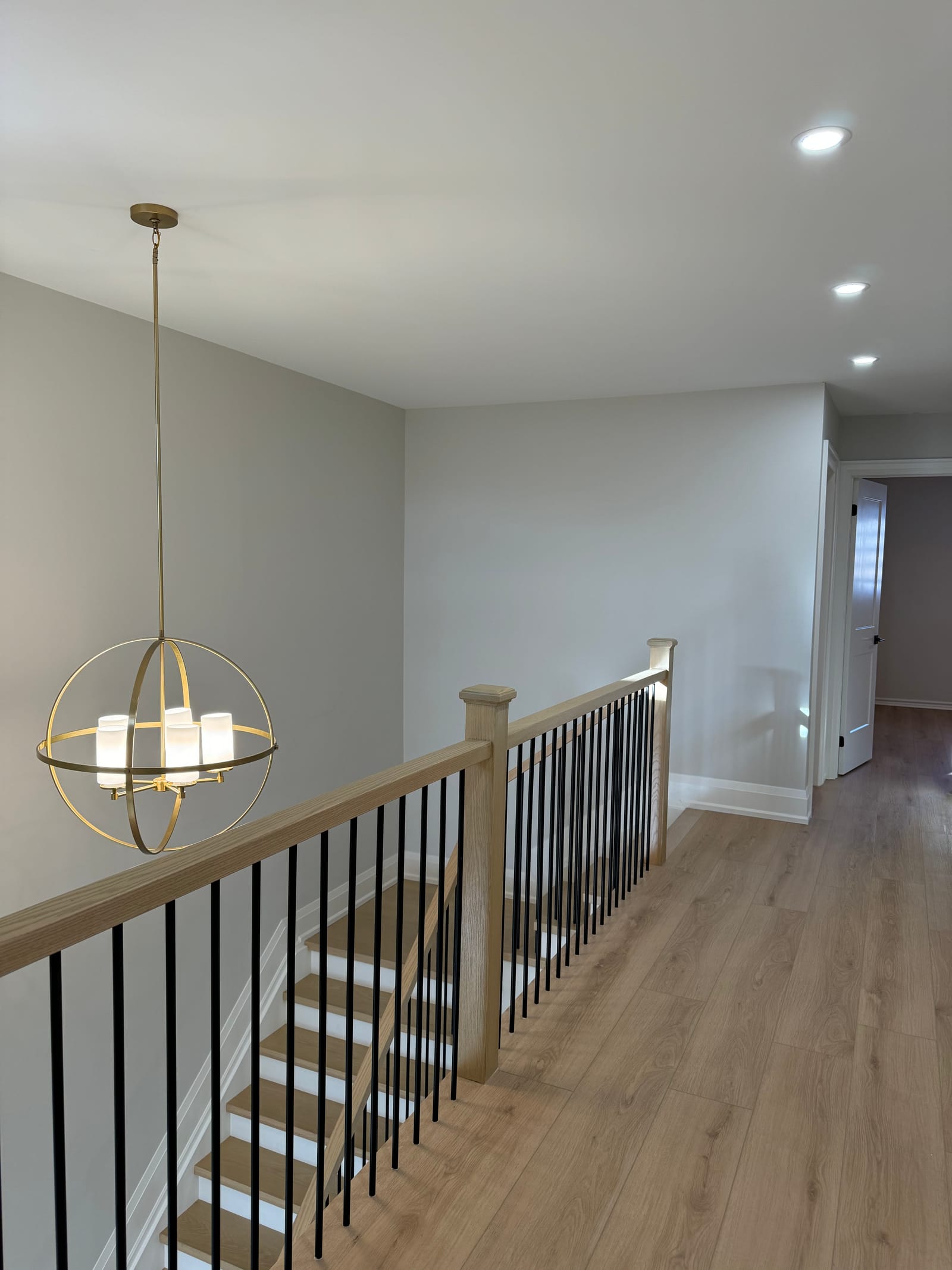An upper hall with an oak stair rail, black spindles and a brass globe chandelier