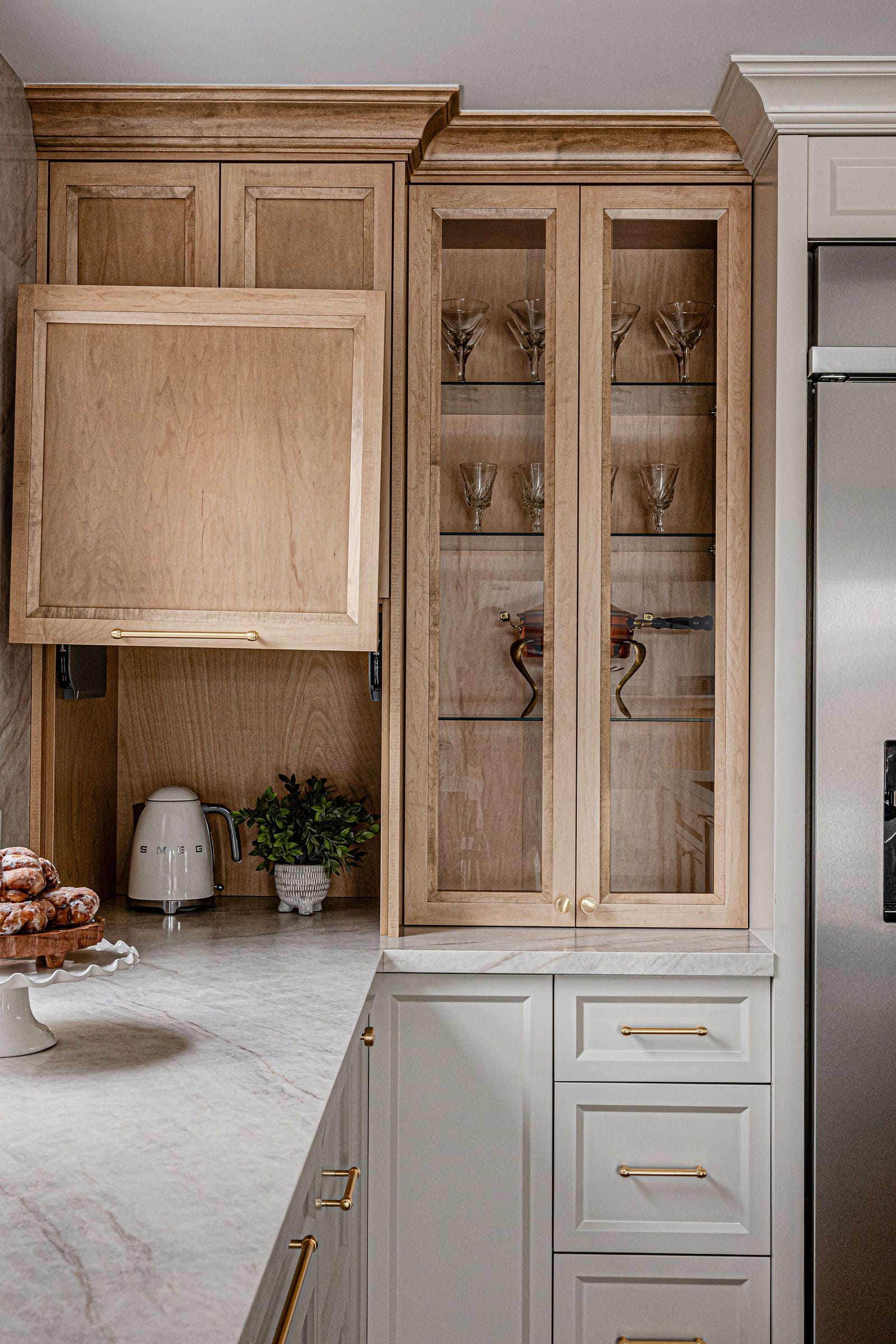 Maple cabinets with a lift-up door over a kettle niche and glass-front cabinets beside a fridge