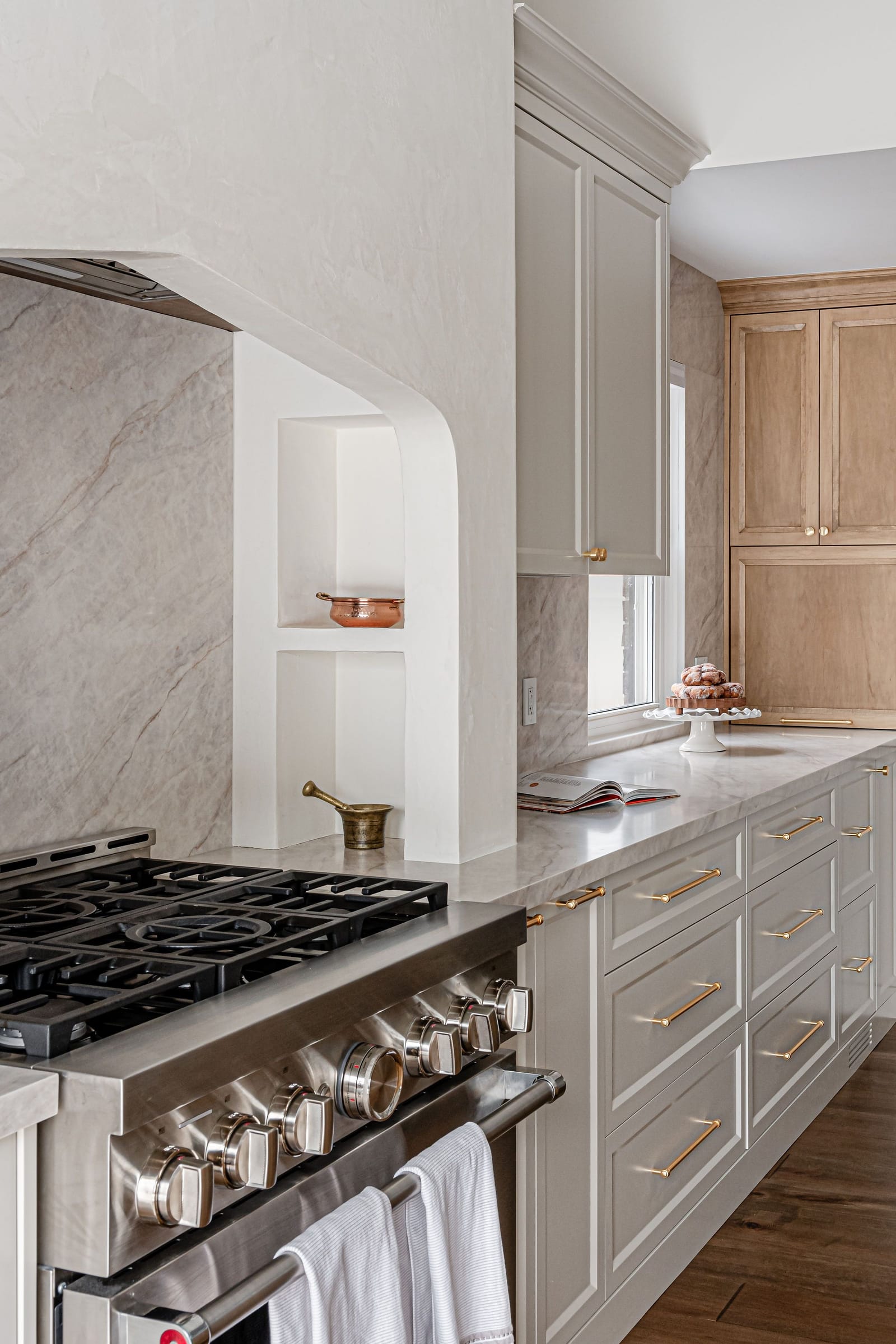 A gas range under the plaster alcove beside a run of cream drawers with brass pulls