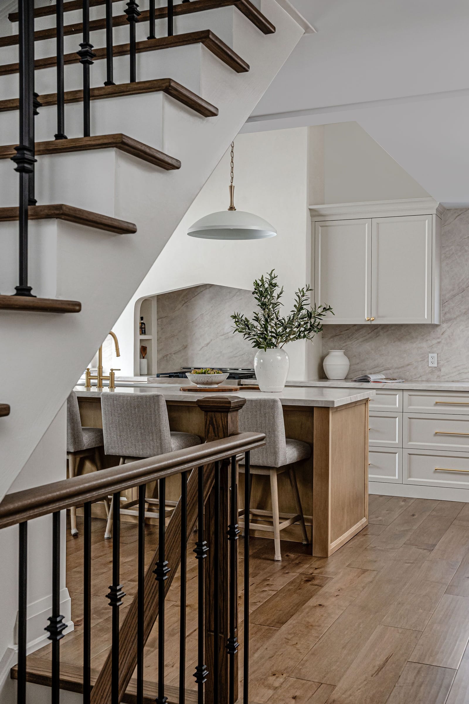 A stair with dark treads and iron spindles looking down onto the kitchen island