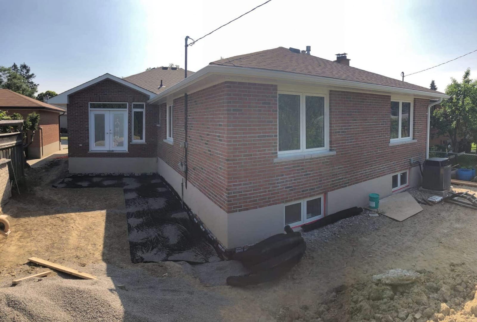 A brick bungalow with a rear addition and French doors, with the yard still dug up for drainage