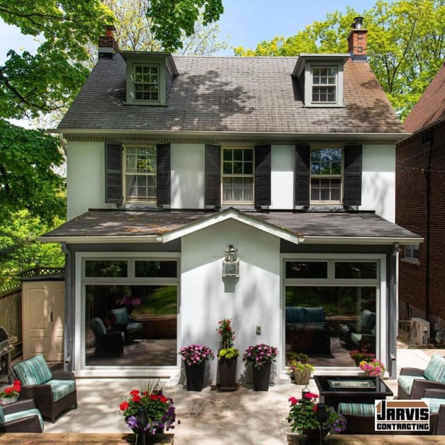 A white stucco house with a ground-floor garden room of tall windows opening onto a patio