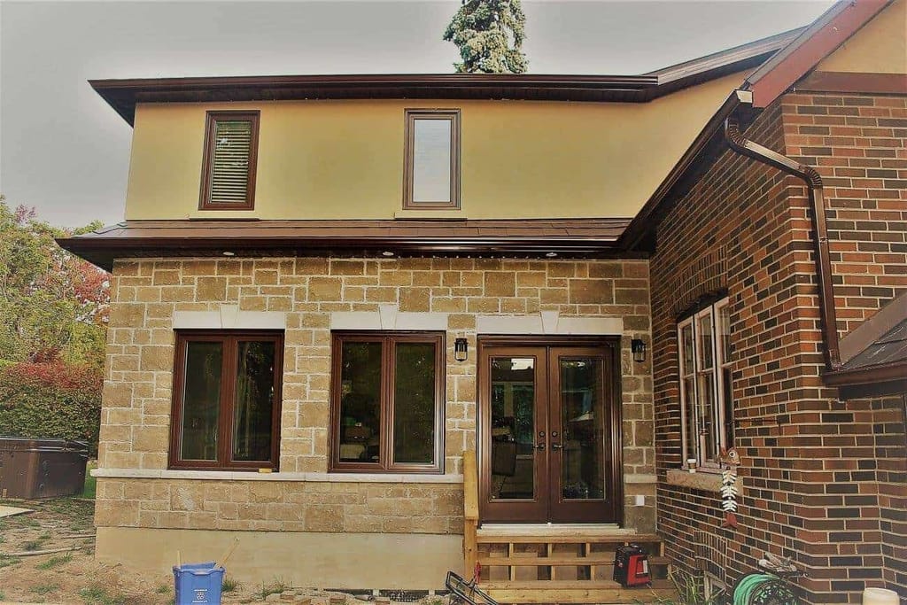 Close view of the addition's cut-stone wall, brown-framed windows and French doors, with stucco above