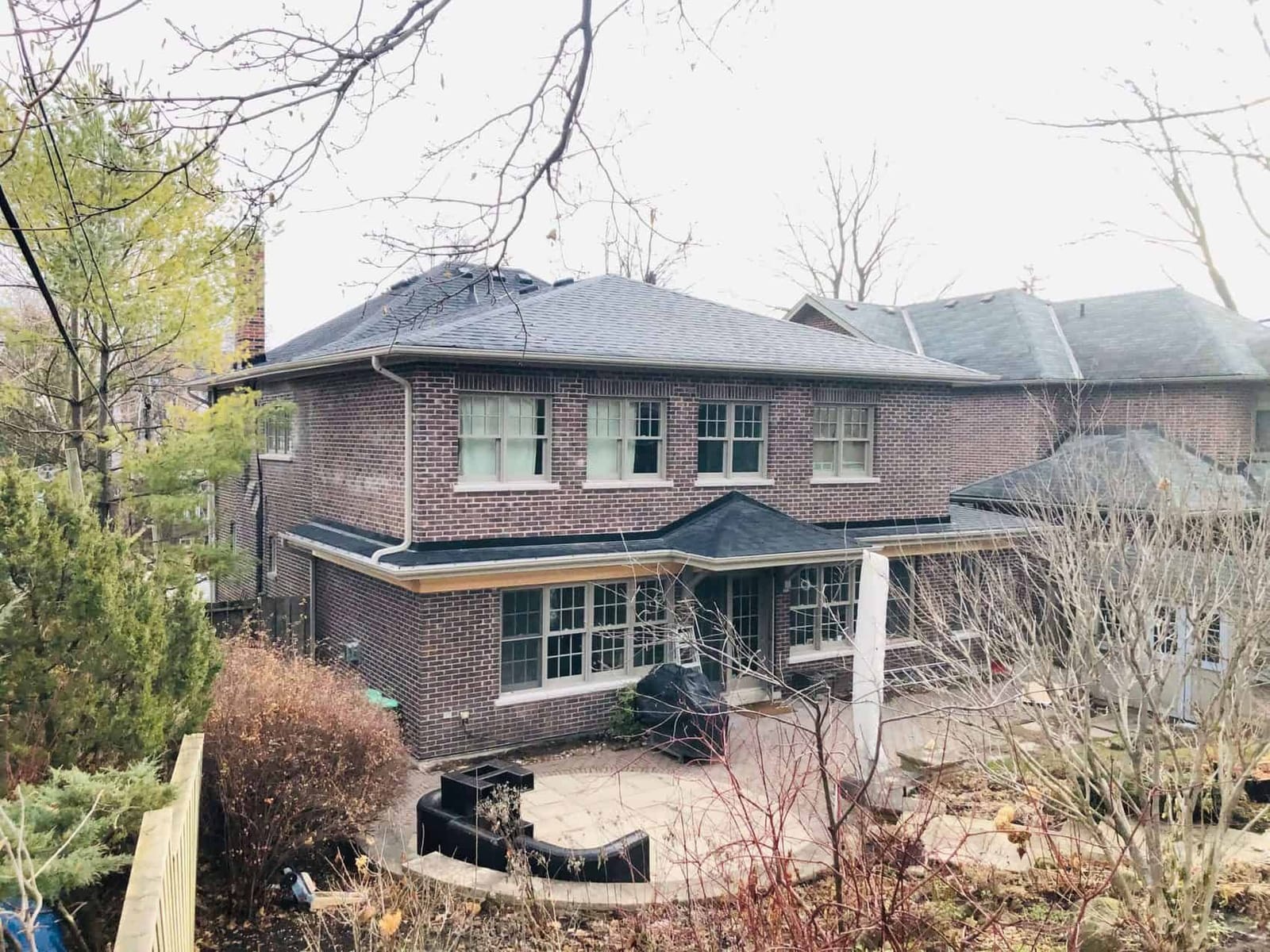 The back of a two-storey brick house with a one-storey extension and a patio, seen from up the garden