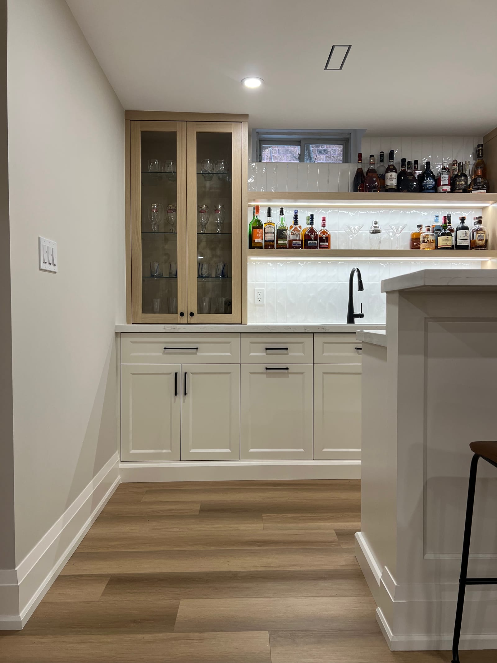 Side view of the bar cabinets and lit bottle shelves under a small basement window