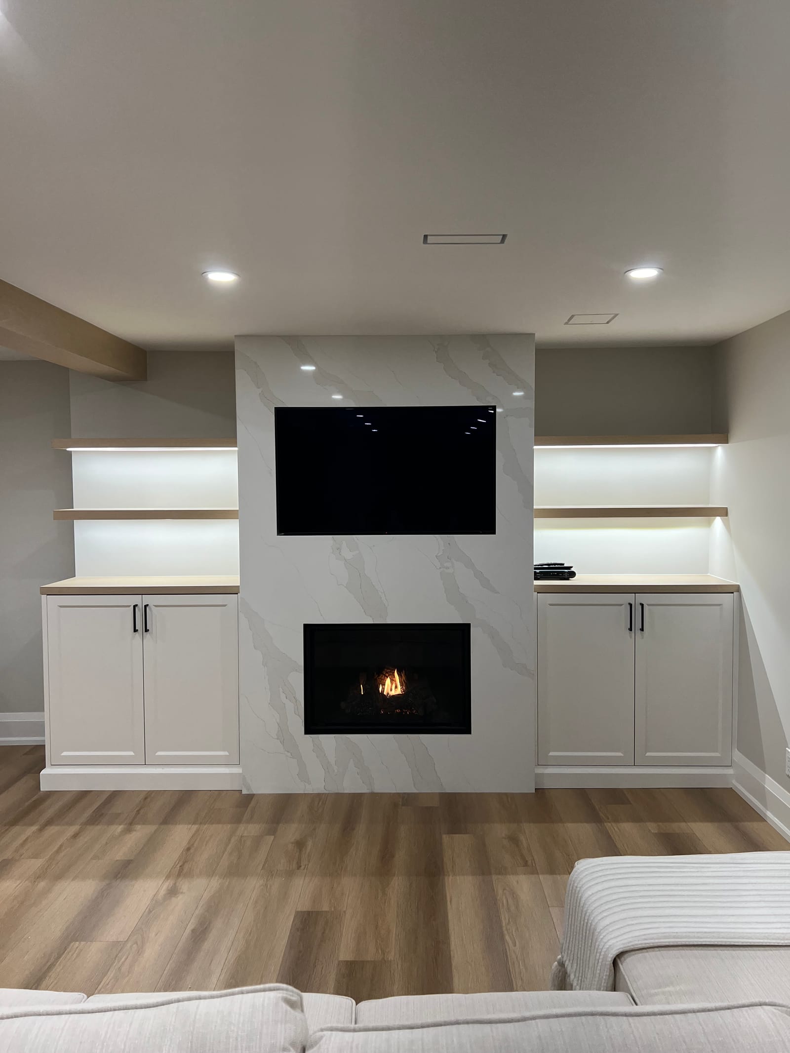 Straight-on view of the stone-clad fireplace and TV wall with lit oak shelves either side