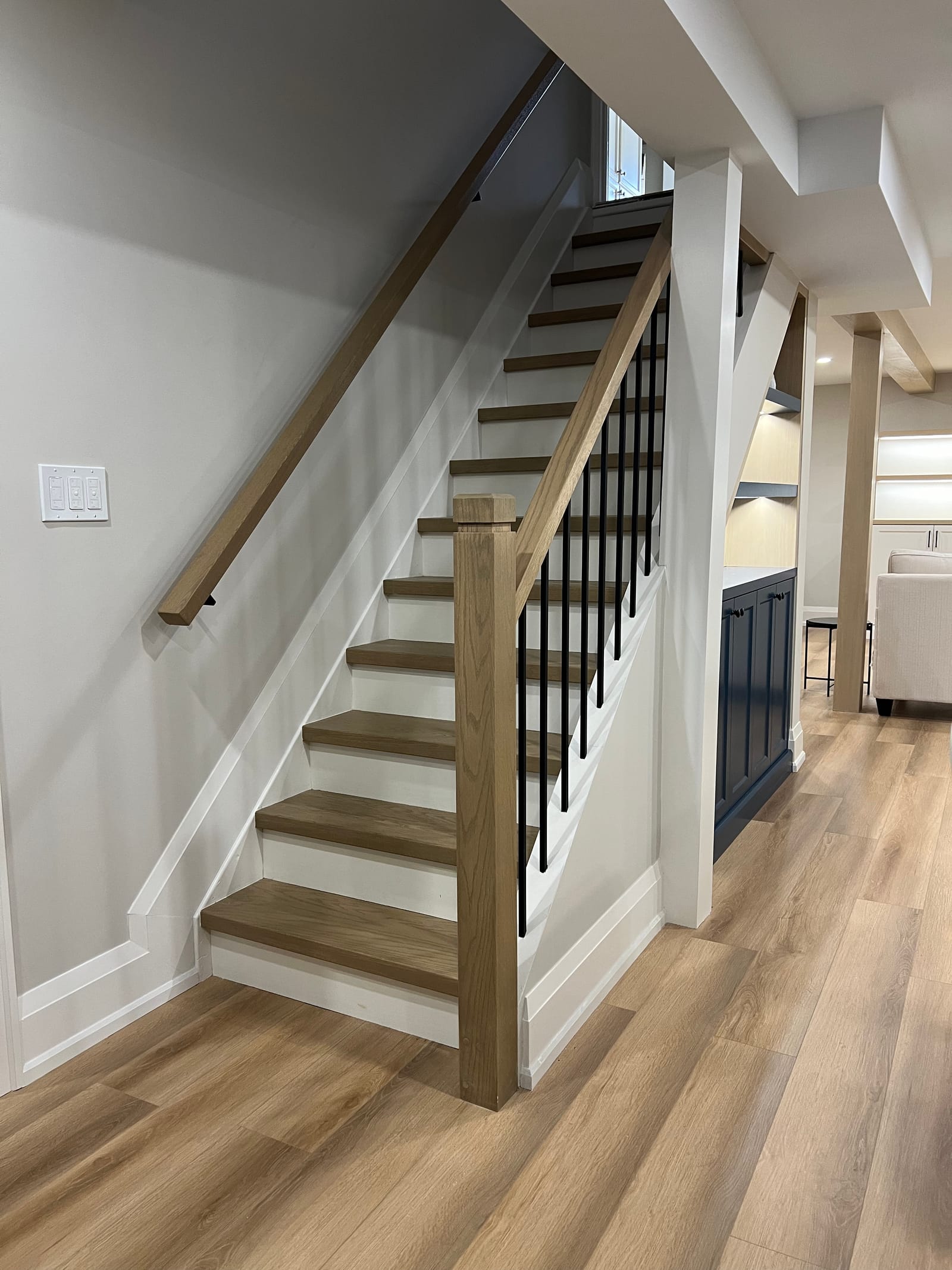 An oak basement stair with a wood handrail and black spindles
