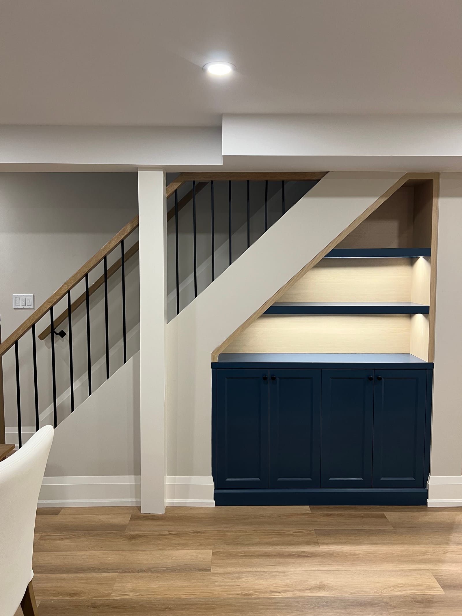 A navy cabinet with lit shelves built into the space under the basement stair