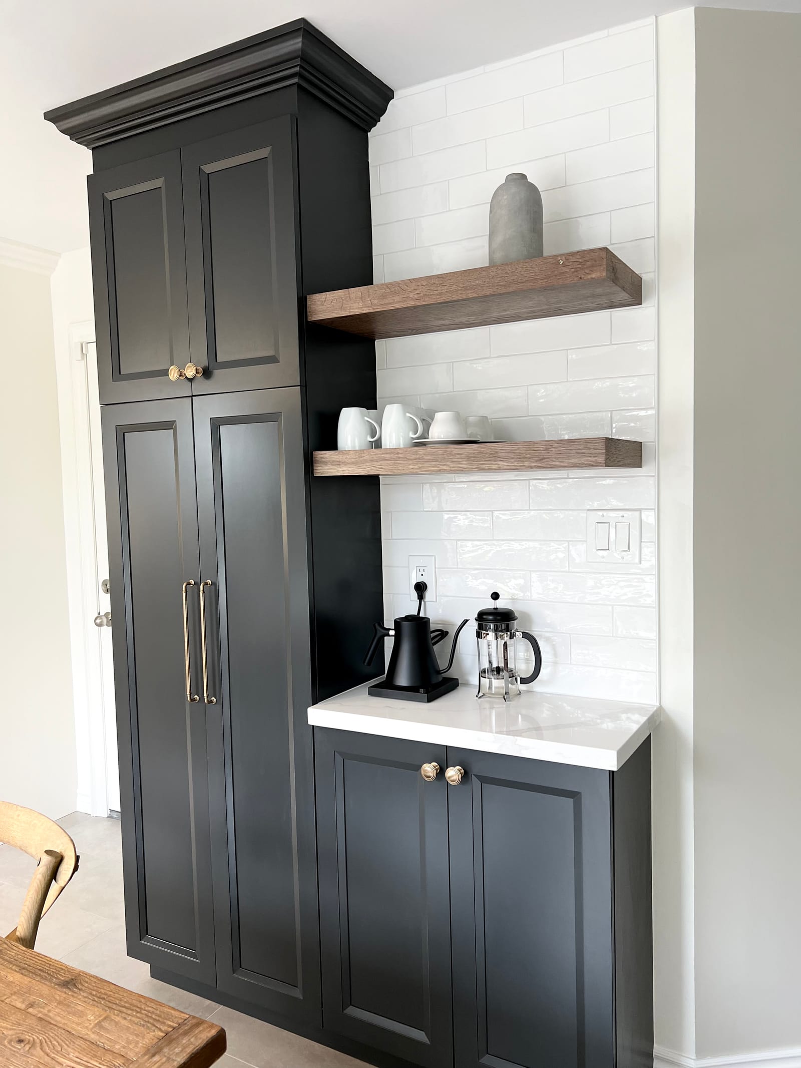 A charcoal cabinet tower with brass knobs and a coffee station under two walnut shelves