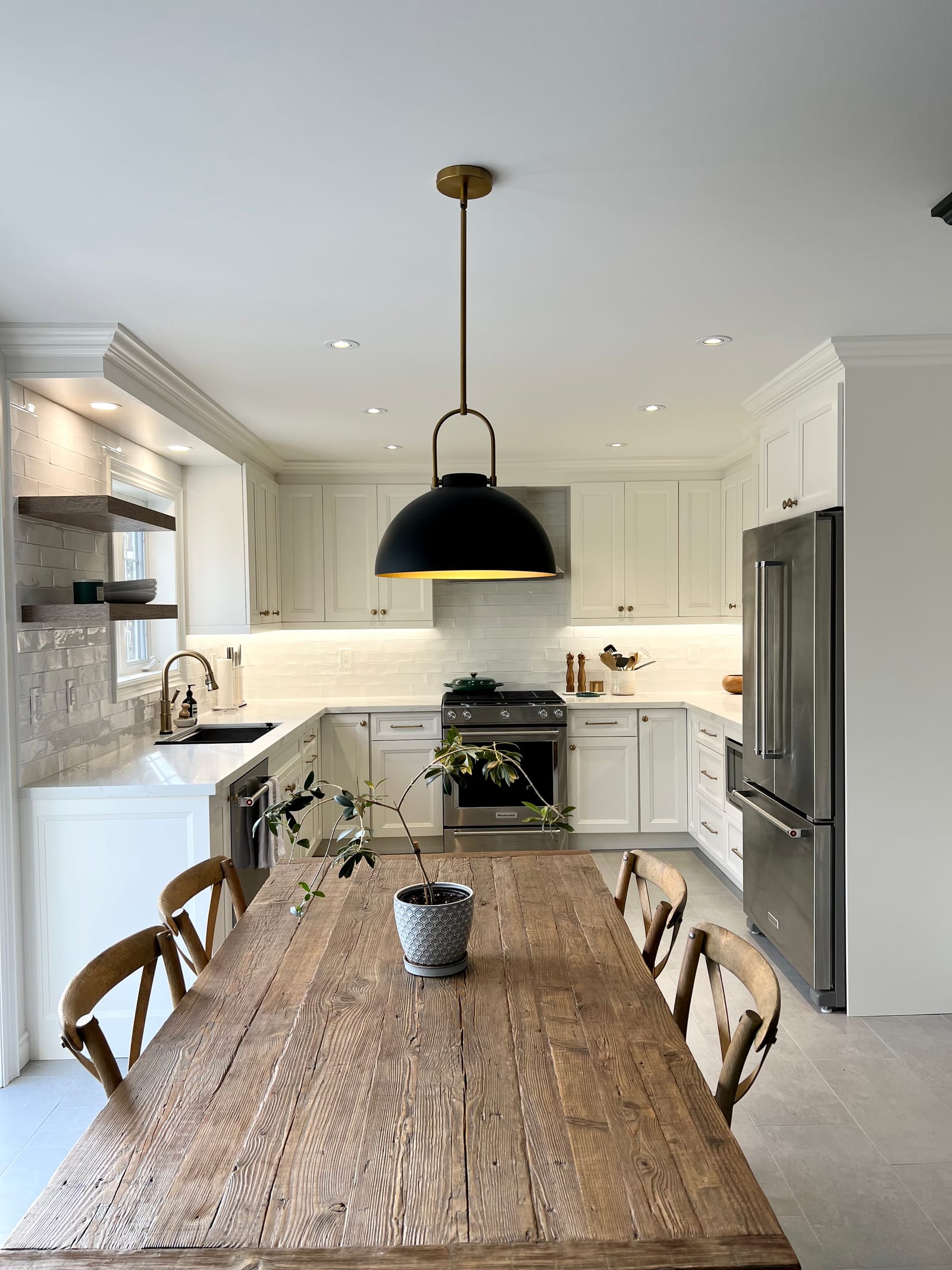 A white kitchen with a rustic plank table, a black dome pendant, open shelves and a gas range