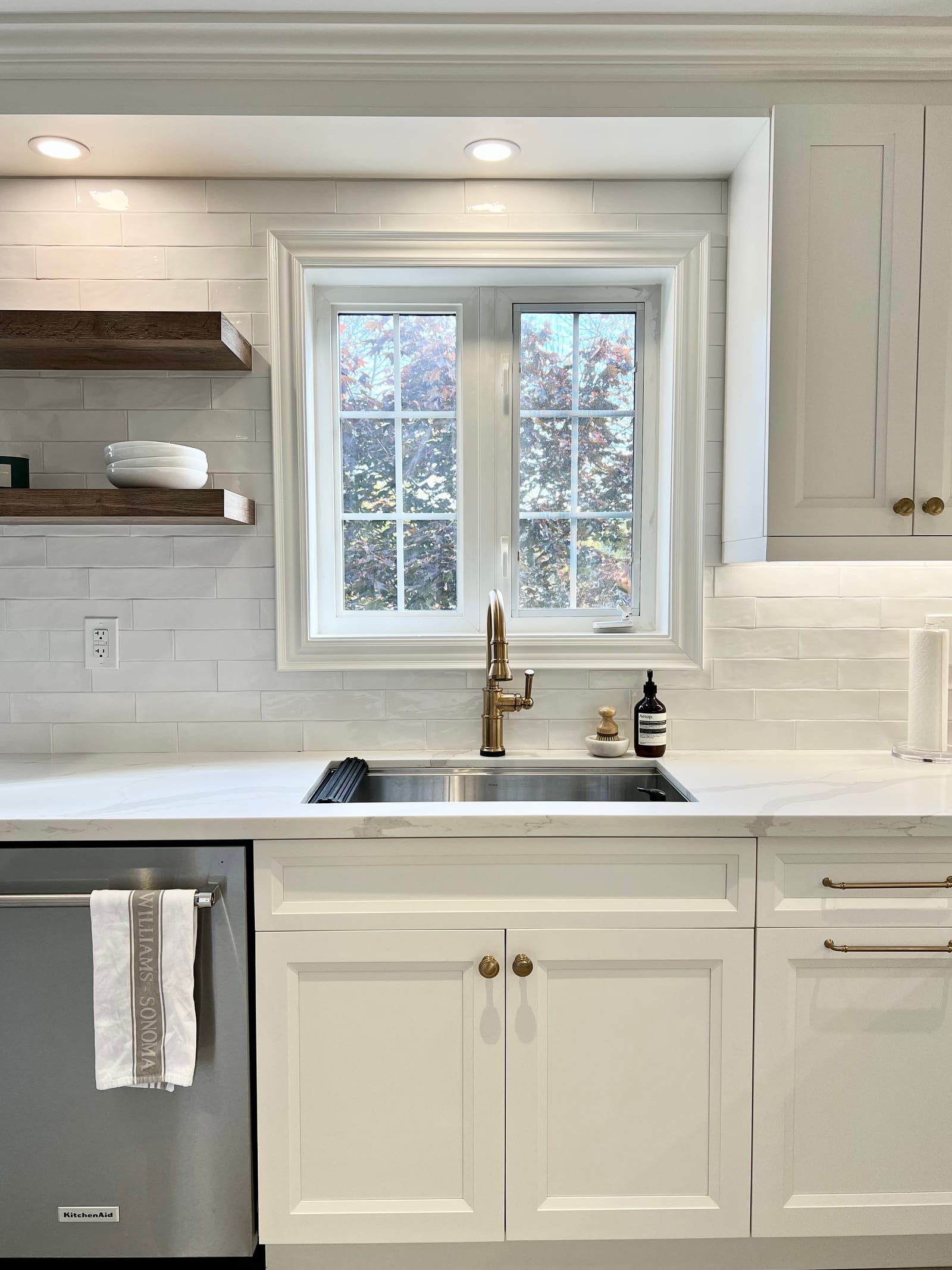 A sink with a brass faucet under a gridded window, with walnut shelves to the side