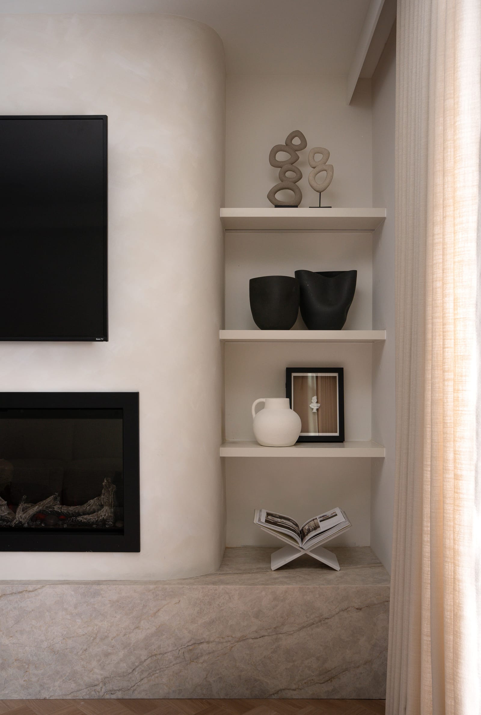 Close view of the lime-washed fireplace wall curving into a niche of open shelves, above a mitred Taj Mahal stone ledge