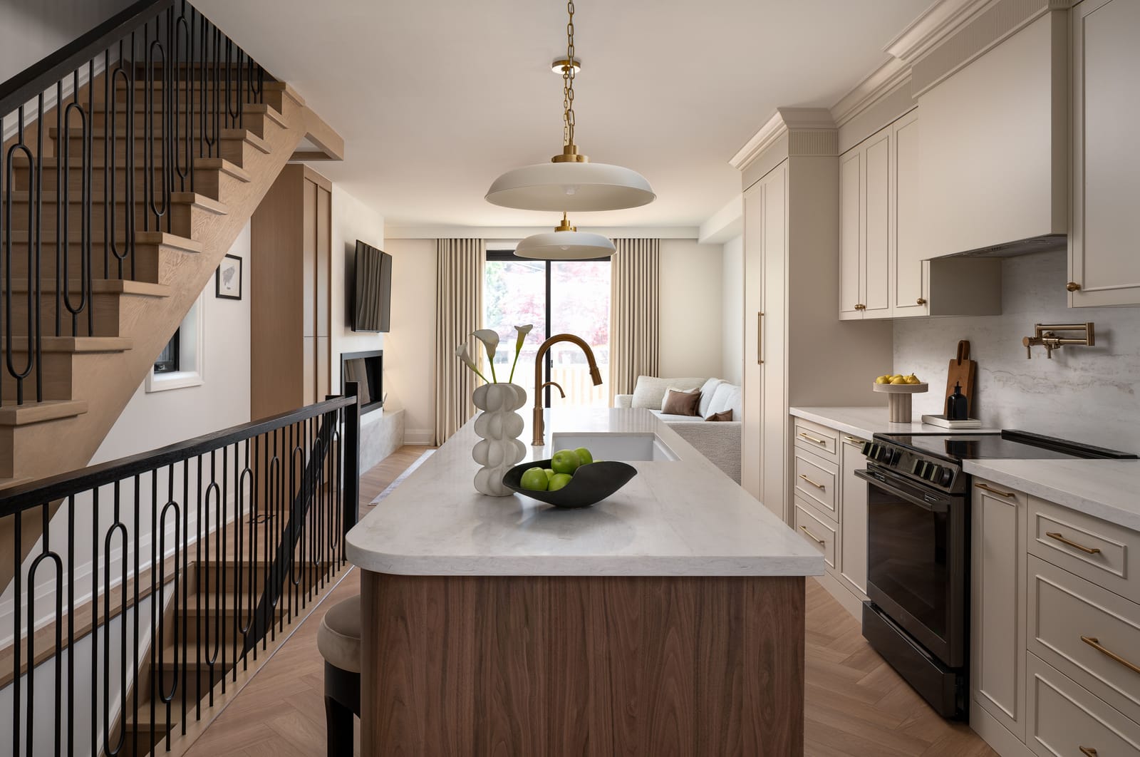 A narrow kitchen with a walnut island beside an open oak stair with black balusters