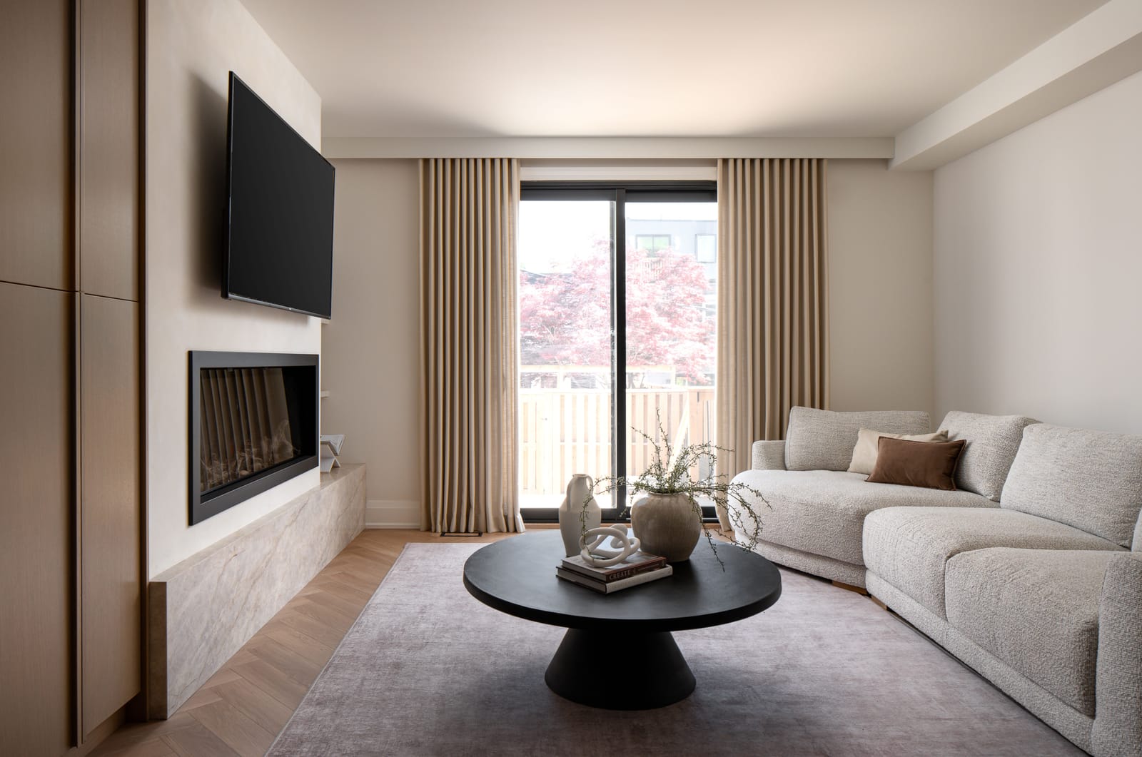 A living room with a linear gas fireplace set in a lime-washed wall over a stone ledge, a boucle sectional and sliding doors to a deck