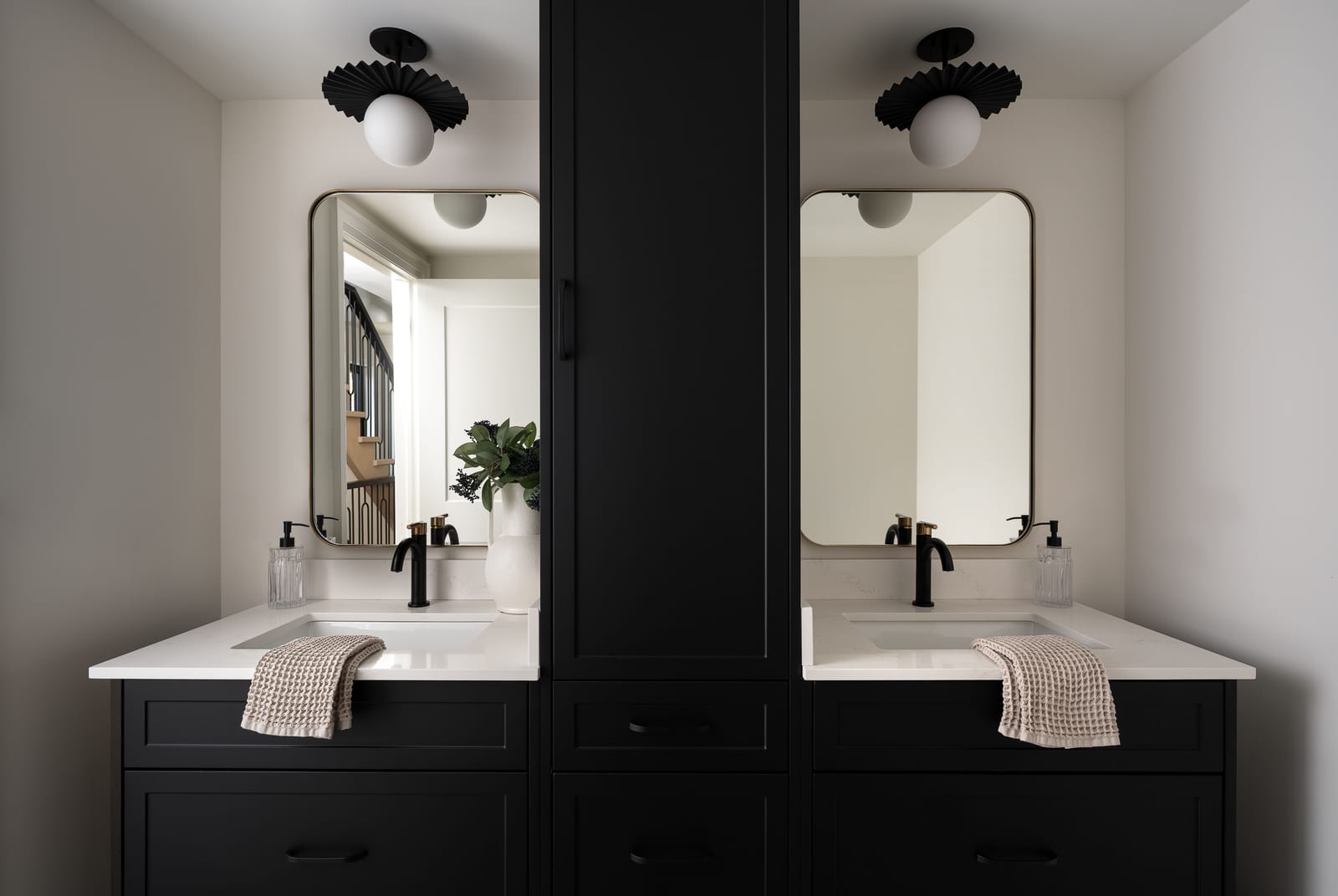 A double vanity in black cabinetry with two round mirrors, white counters and matte black taps, under two globe ceiling lights