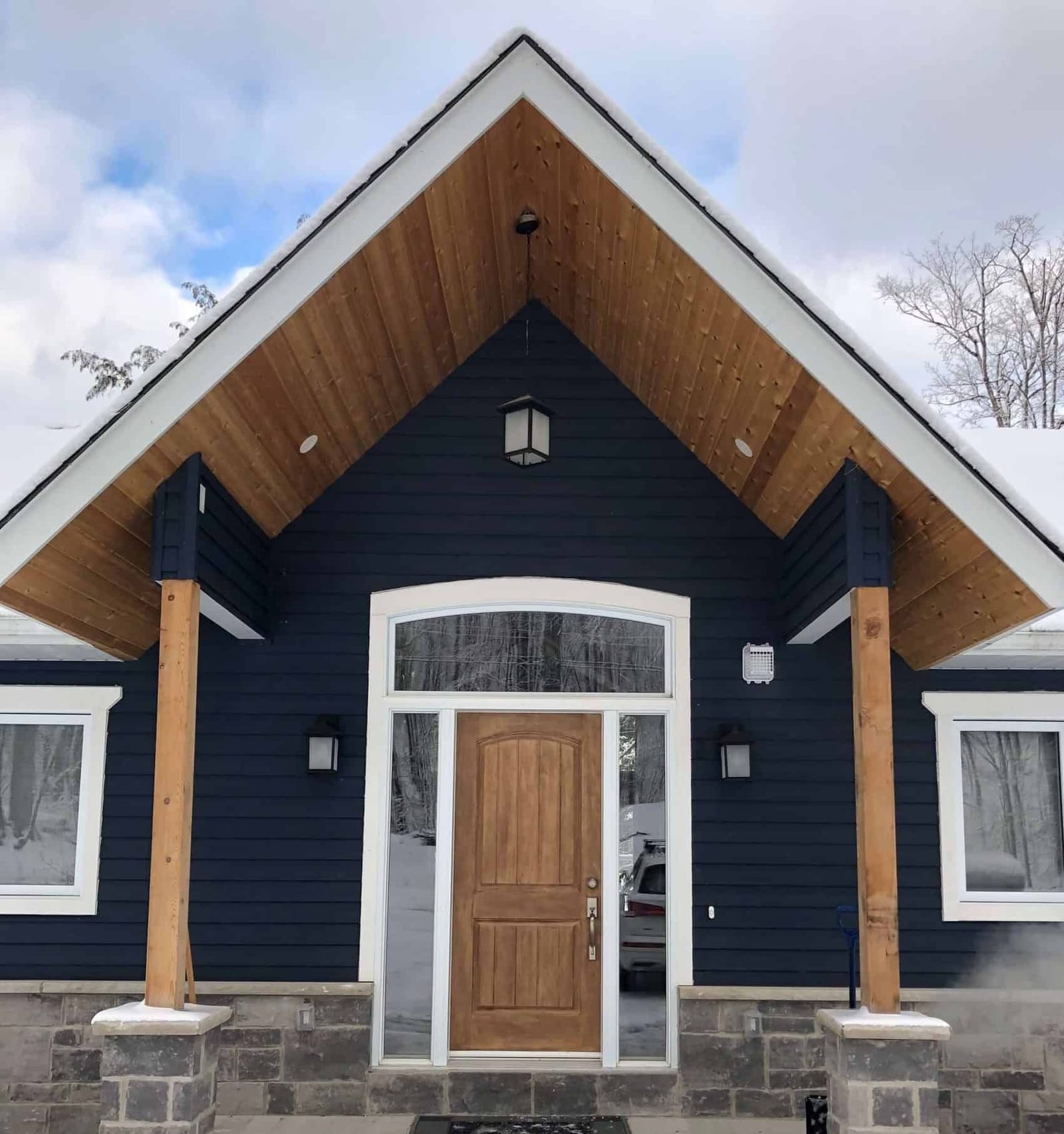 A timber-posted entry porch with a cedar-lined gable over a wood front door and transom