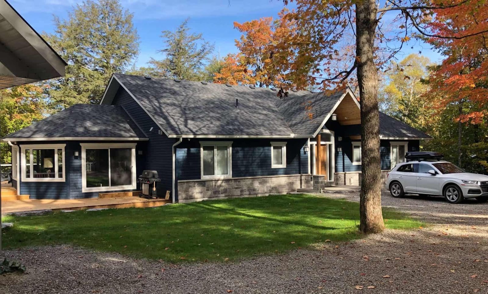The front of a navy single-storey house with stone skirting, a timber entry gable and a gravel drive in autumn