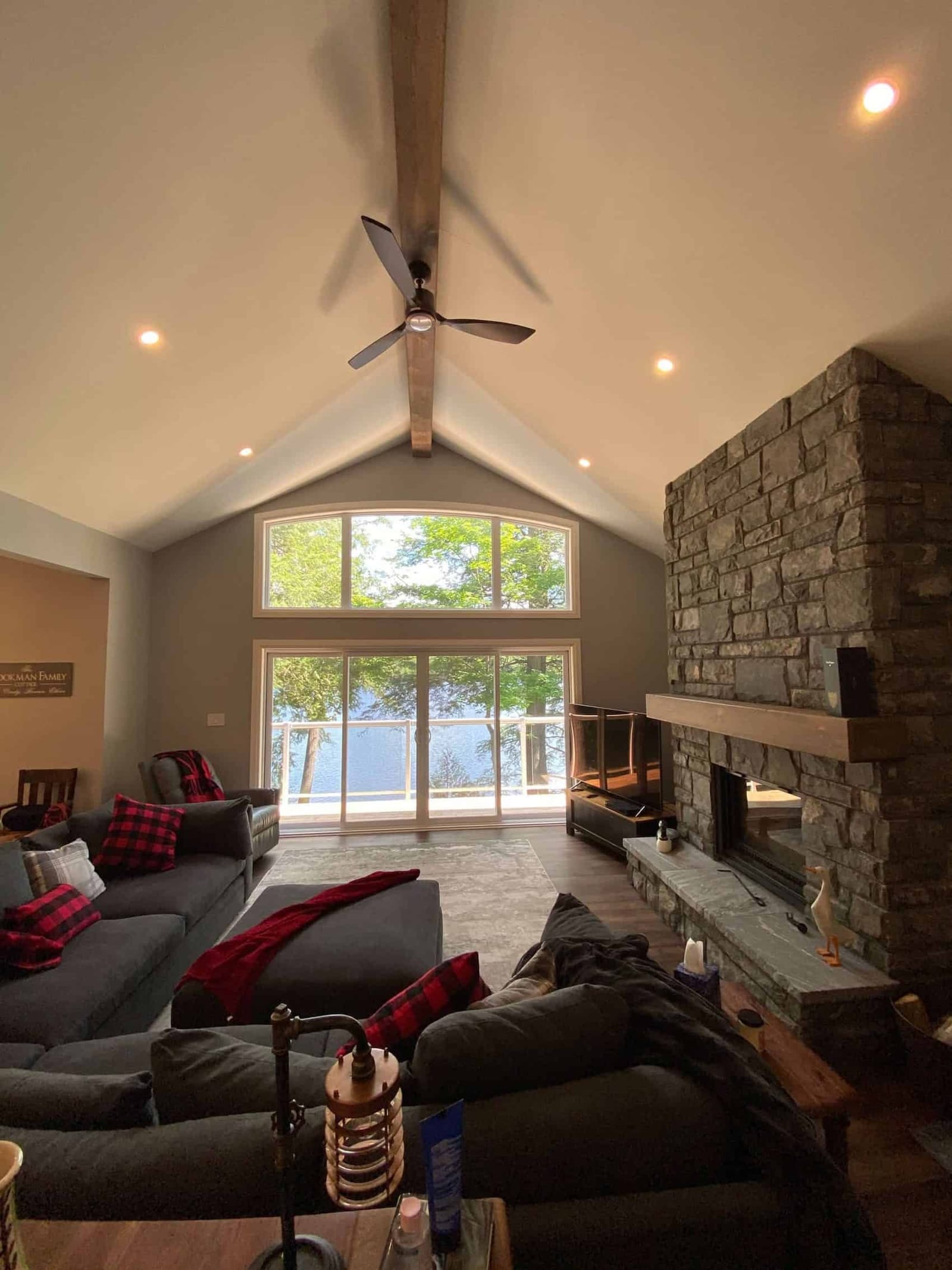 A great room with a vaulted ceiling, a stone fireplace to the ceiling and tall windows facing the lake