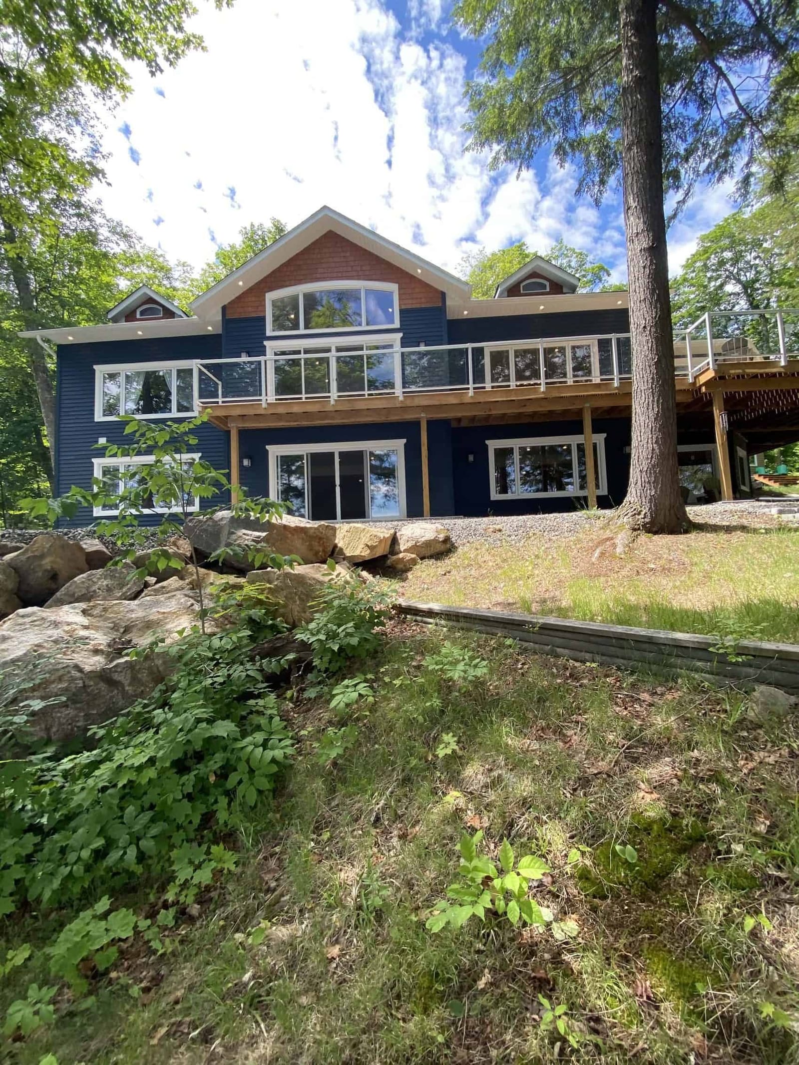 The lake side of a navy-sided house with a gable window, a long deck with glass railings and a walkout lower level
