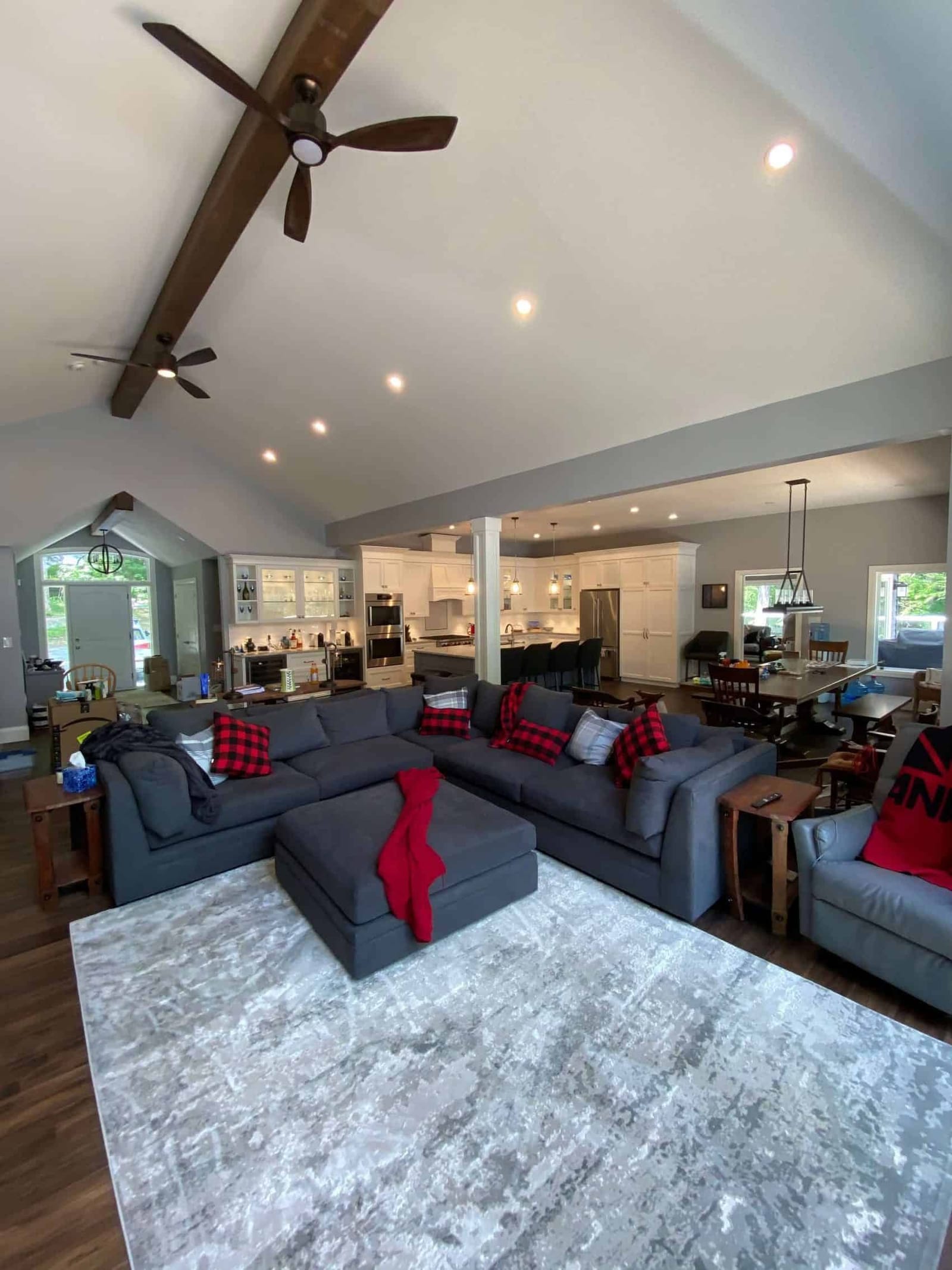An open living, dining and kitchen space under a vaulted ceiling with a dark beam and ceiling fans