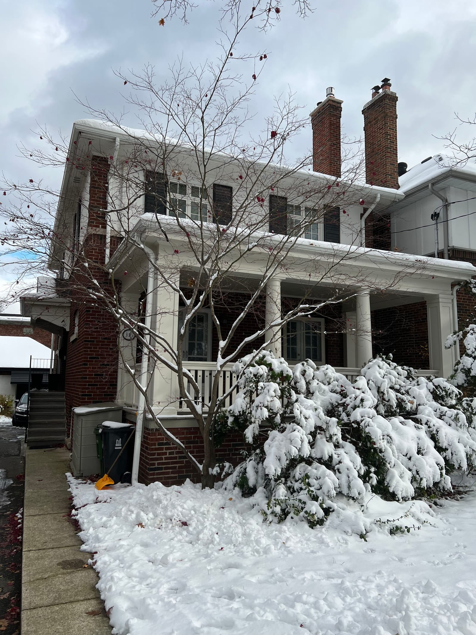 A two-and-a-half-storey brick house with a columned front porch, in snow