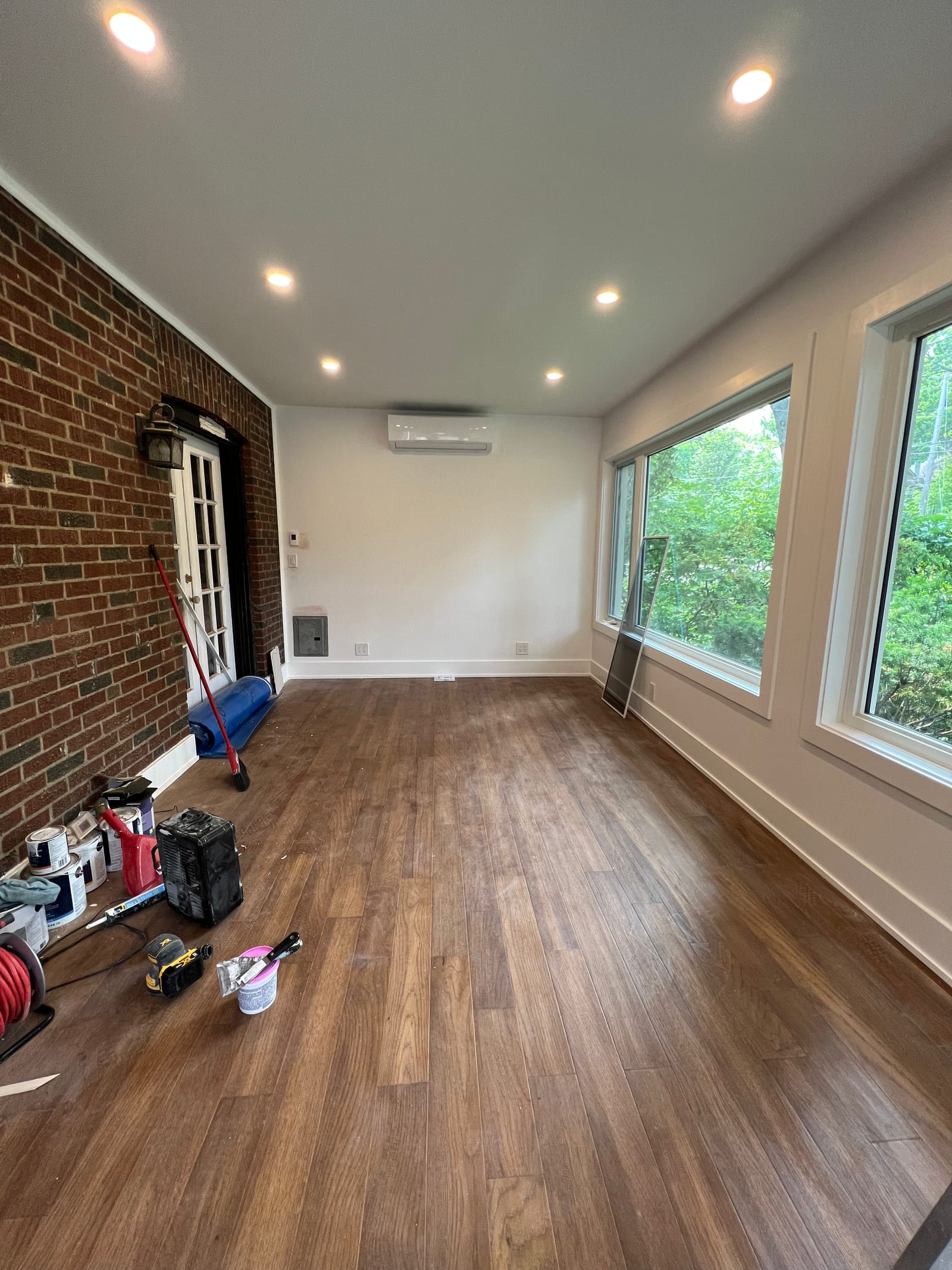 A narrow room with an exposed brick wall, French doors and wide windows, with tools still on site