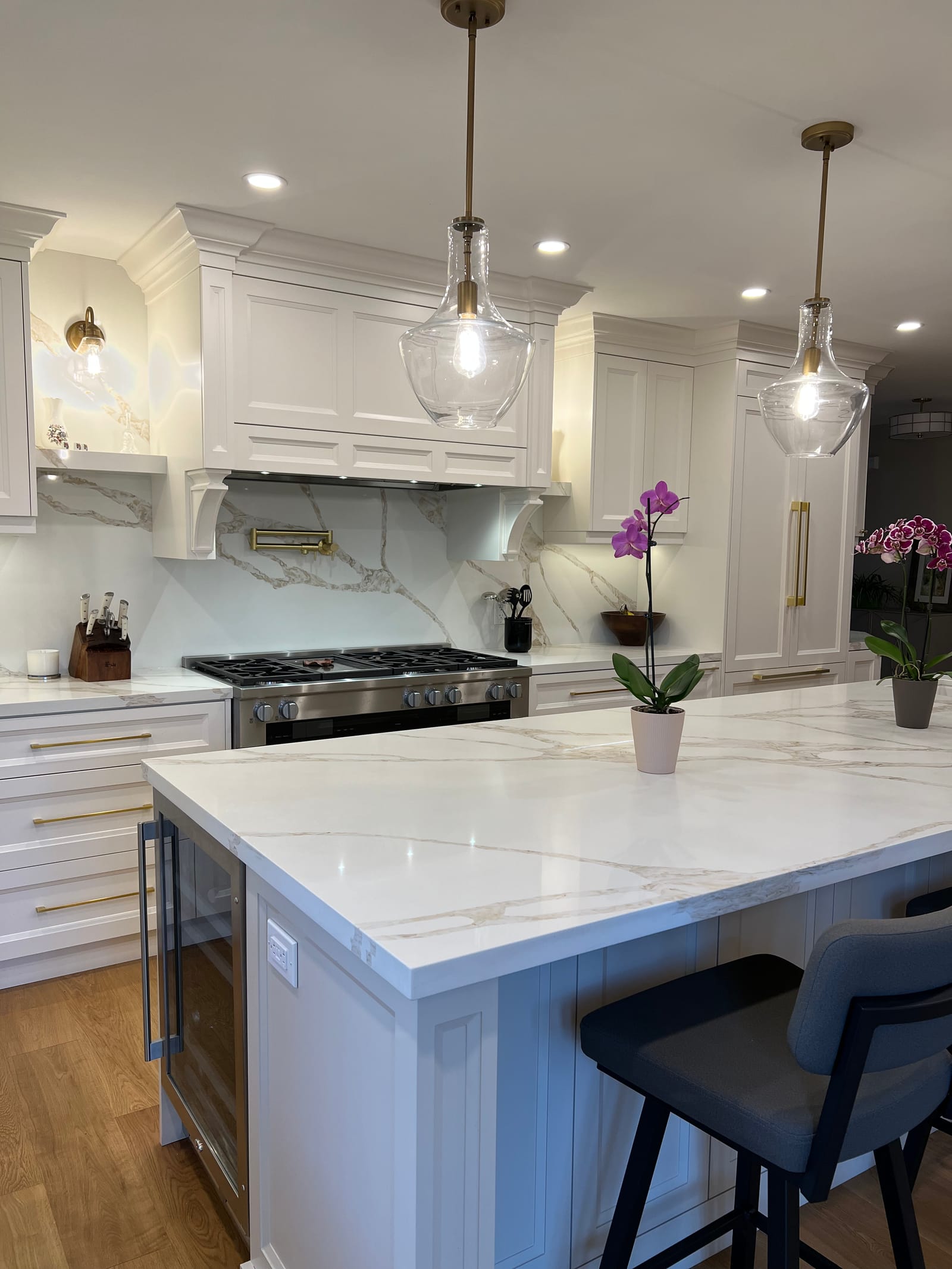 The island with stools in front of the panelled hood and glass pendants