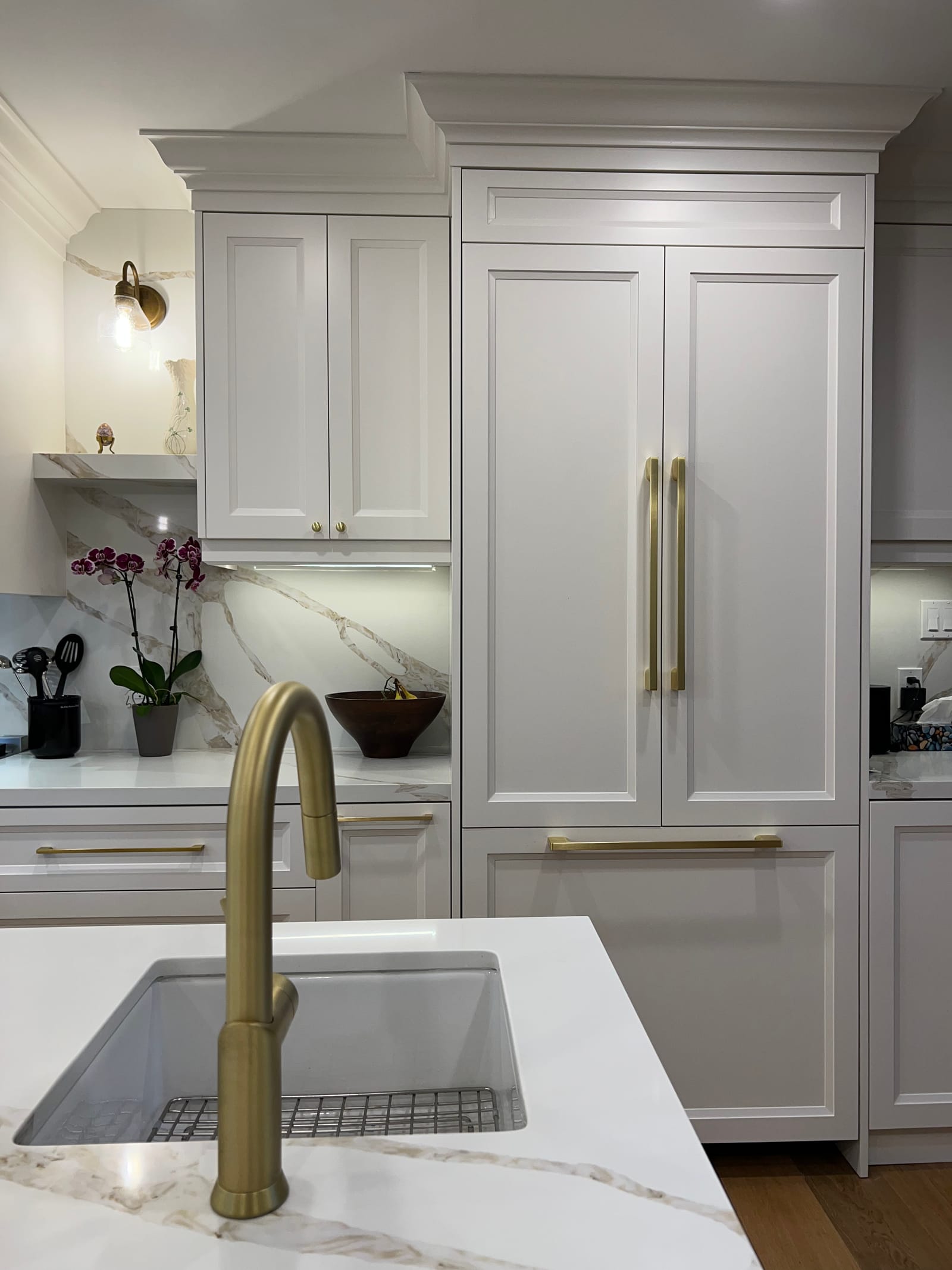 A panelled fridge with long brass pulls beside the island sink and brass faucet