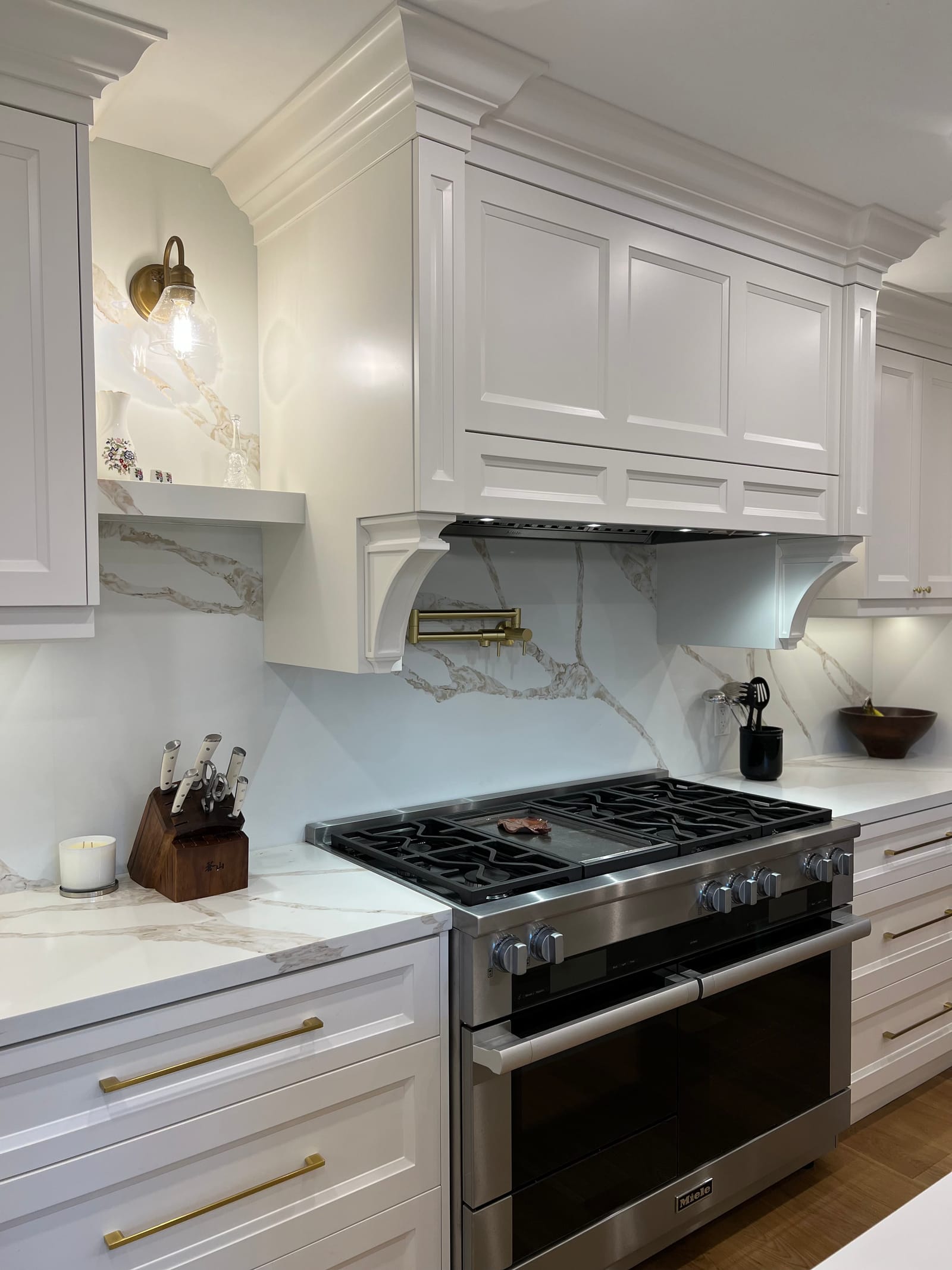 A panelled white hood with corbels over a professional range and a gold-veined slab backsplash