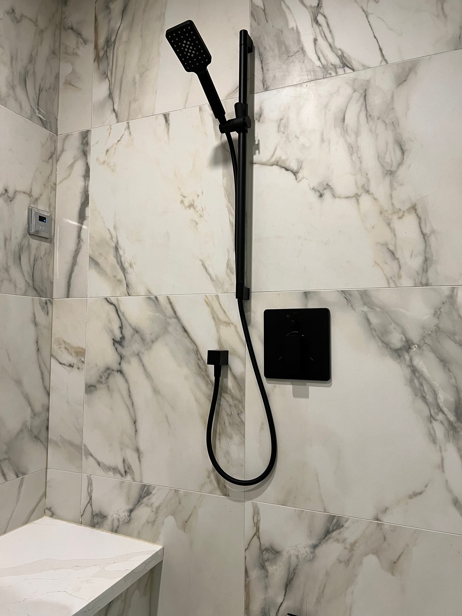 A black hand shower on a slide bar against large marble-look slab tile