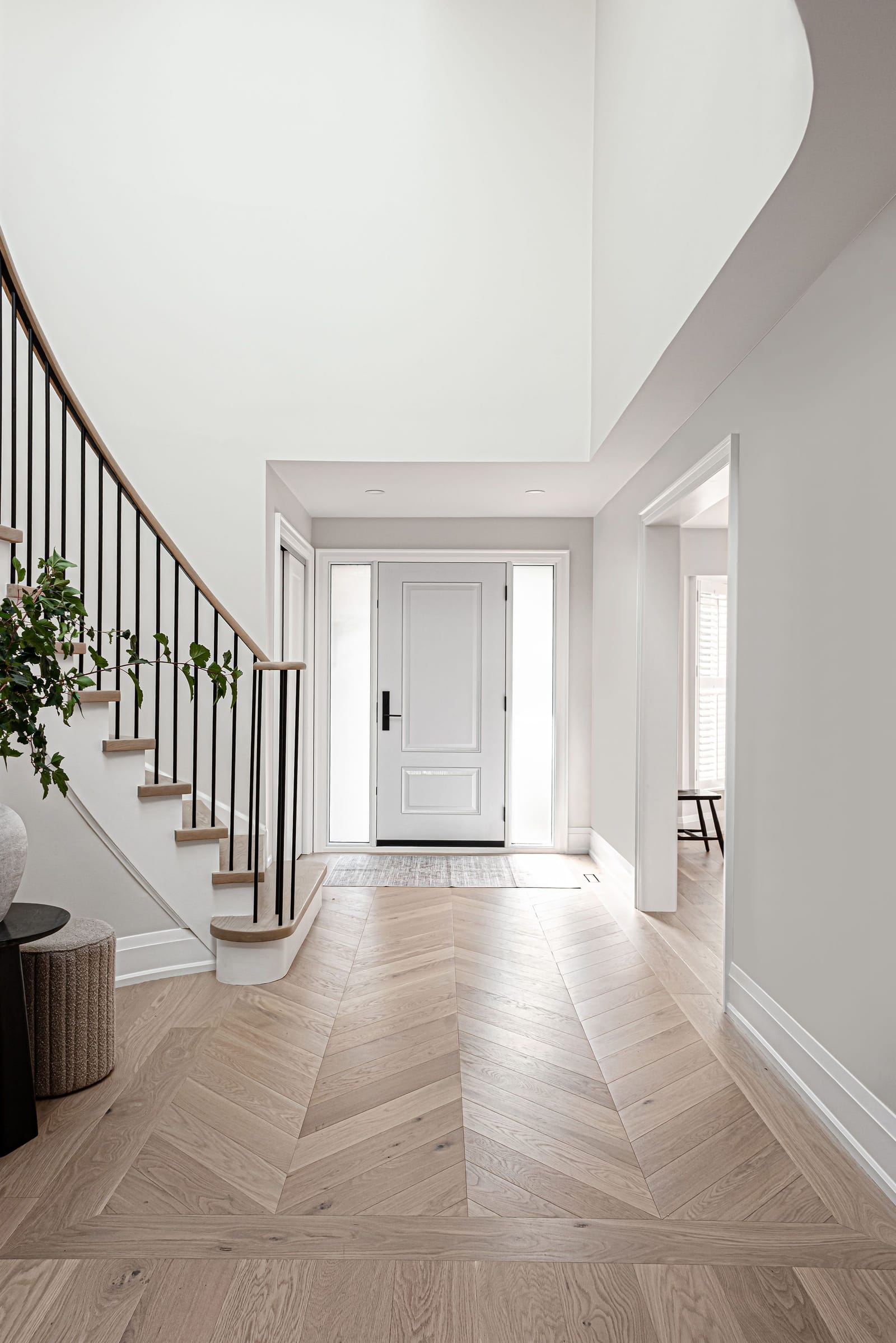 A double-height front hall with a chevron oak floor running to the front door, framed by the sweep of the curved stair