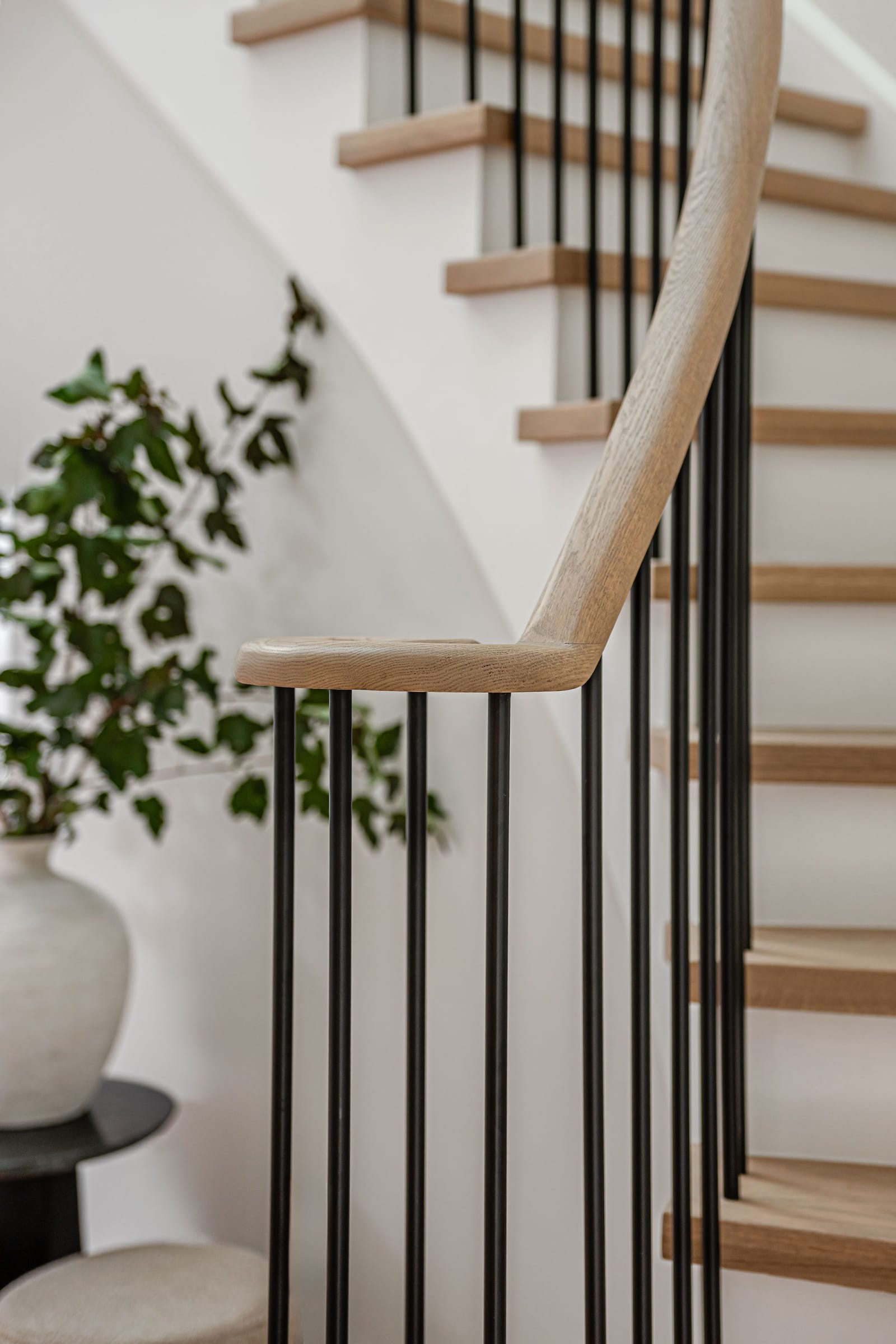 Close view of a curved white oak handrail turning down over black metal spindles and oak treads