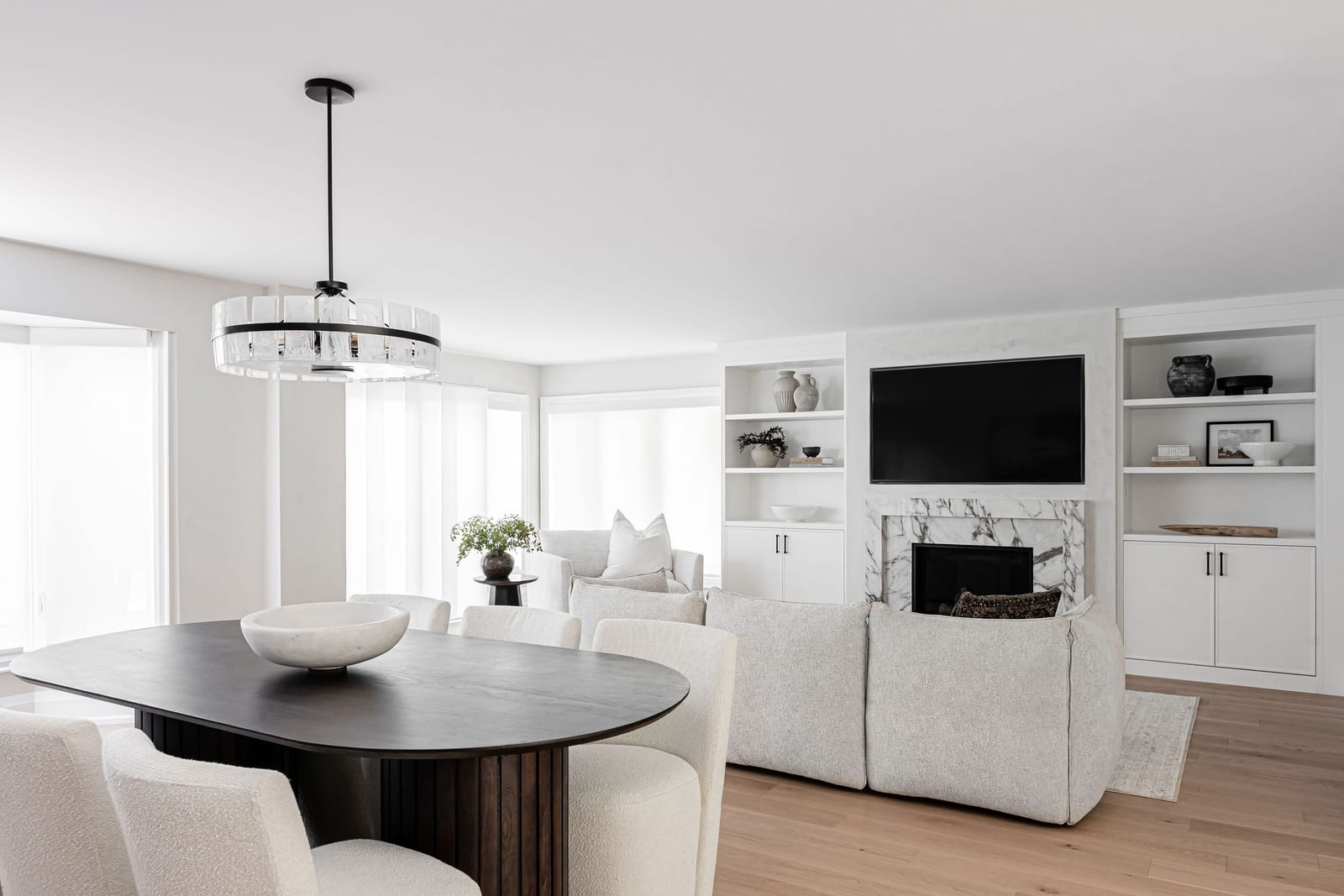 An open living area with a boucle sectional, a fireplace in white veined stone between white built-ins and a television above