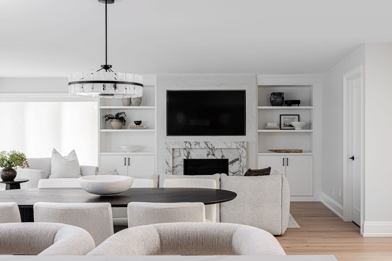 The living wall straight on: white built-ins with styled shelves either side of the veined stone fireplace, behind a sectional and dining table