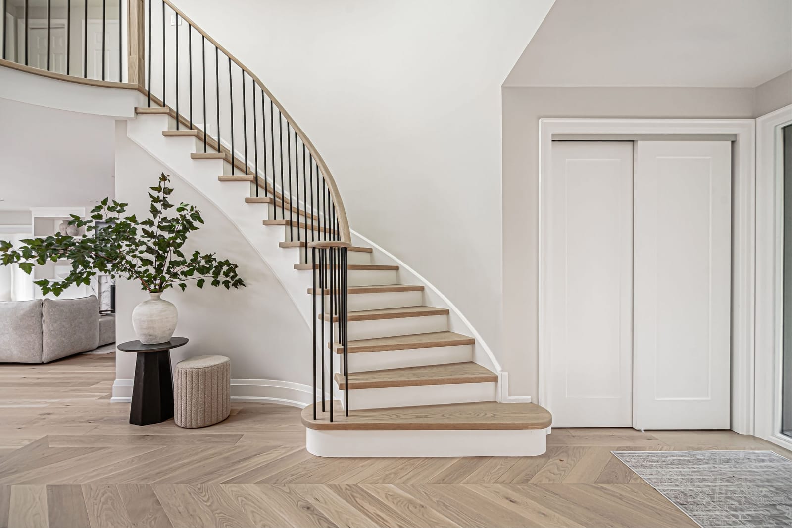 The curved staircase from the side, with a bullnose bottom step, oak treads and white risers, beside a closet with sliding doors