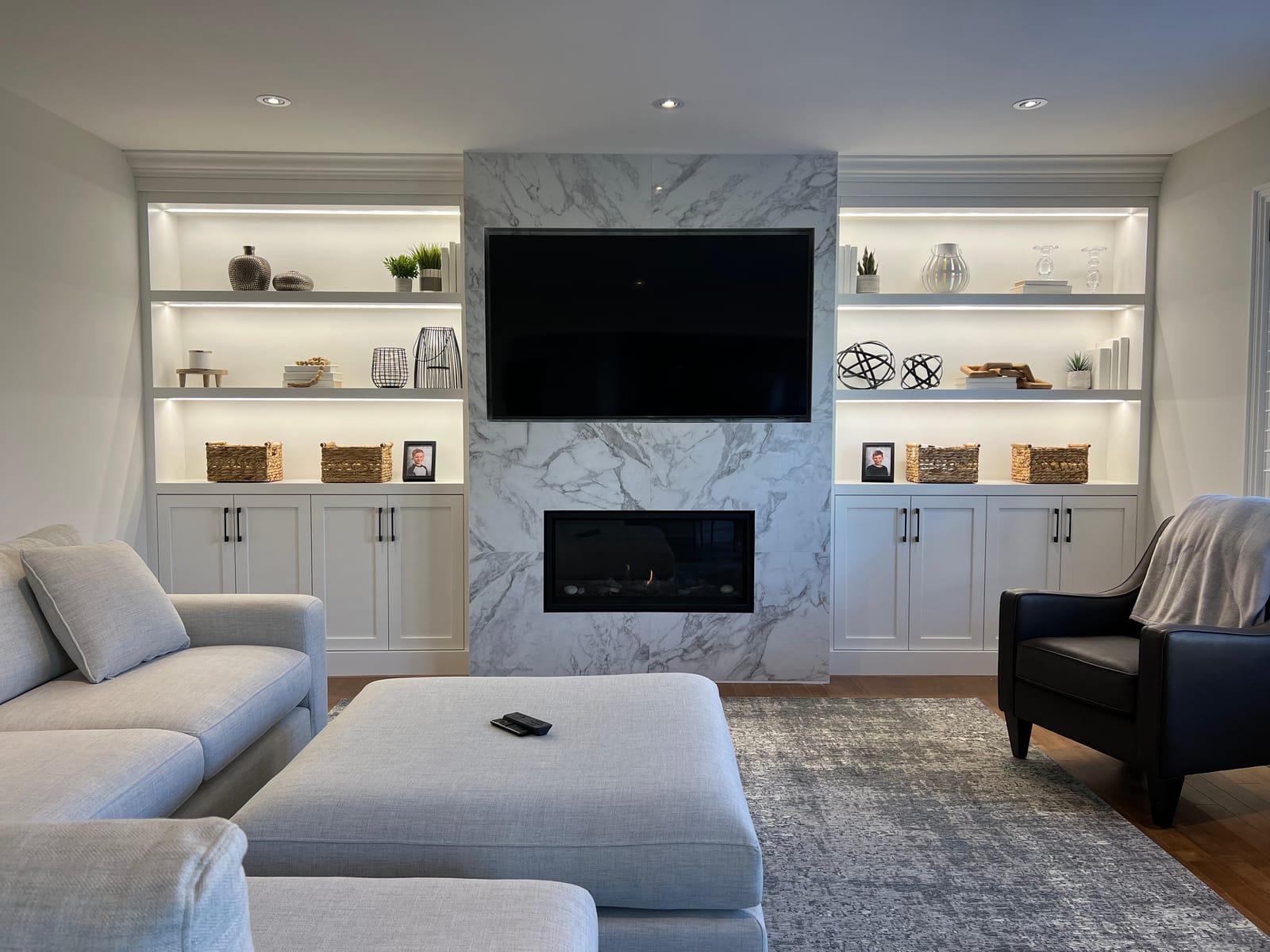 A family room with a marble-look fireplace and TV wall between lit white built-ins, and a sectional