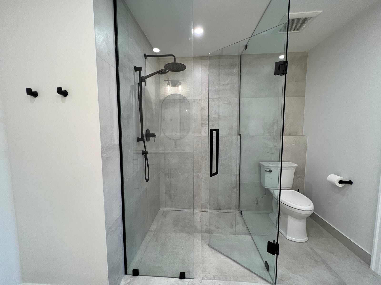A frameless glass shower in large grey tile with black fixtures