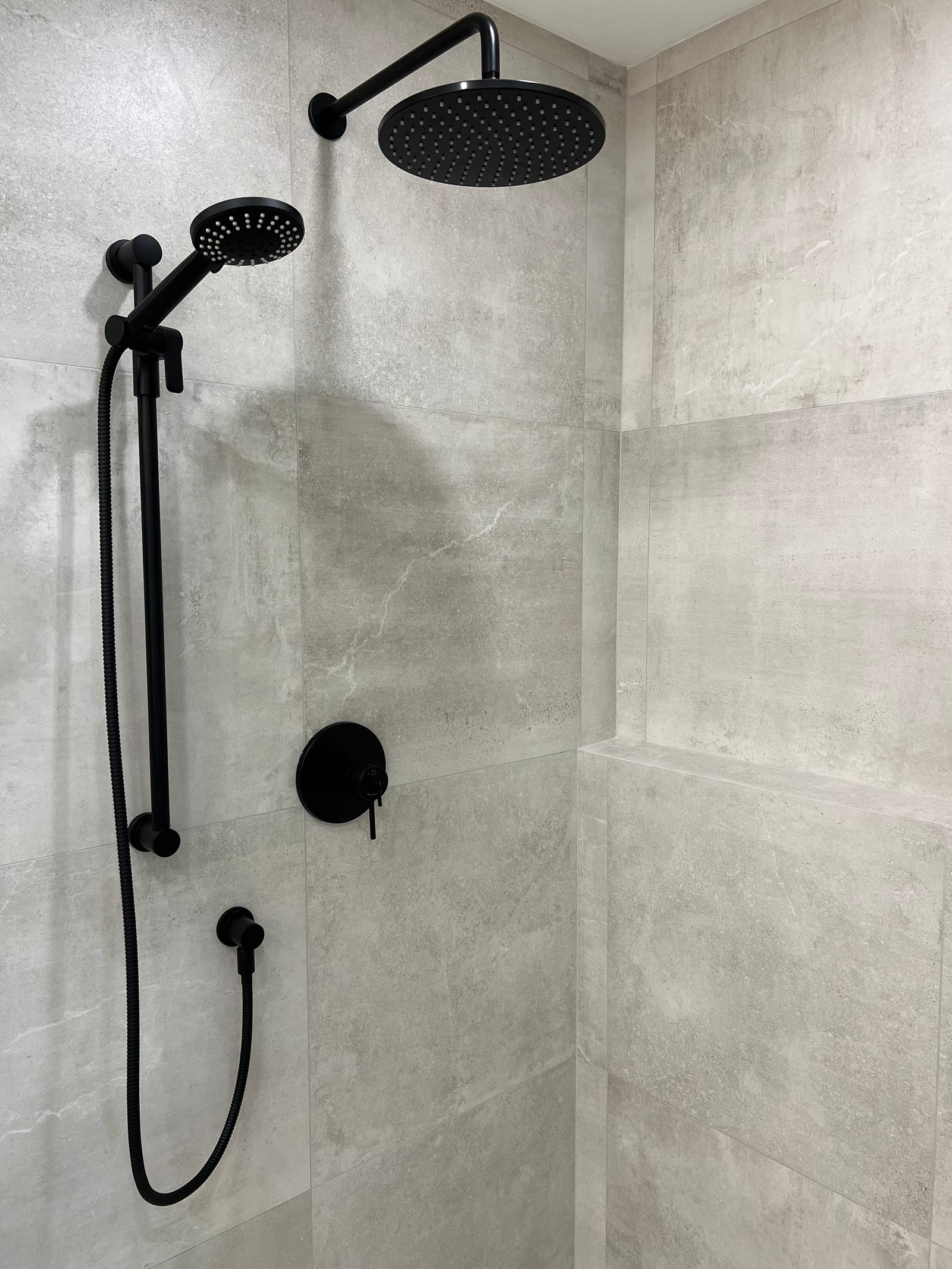 A black rain shower and hand shower against large grey stone-look tile
