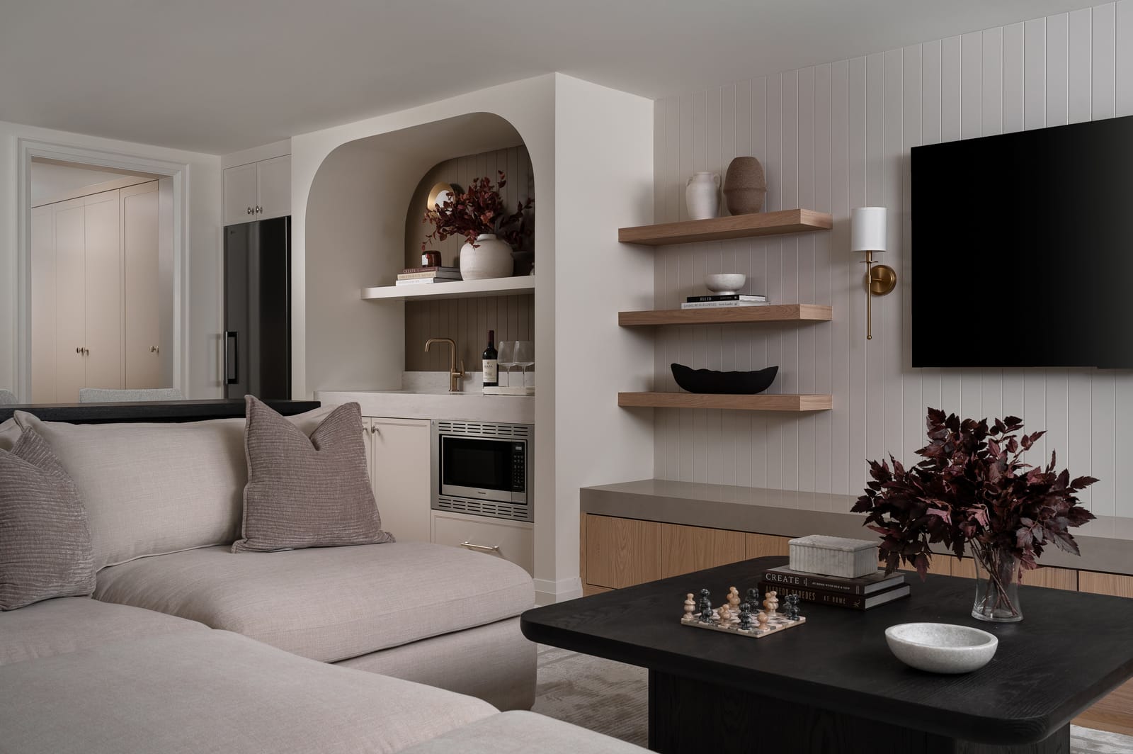 The rec room seen from the sectional, with the media wall on the right and an arched wet bar with a microwave and sink at the back