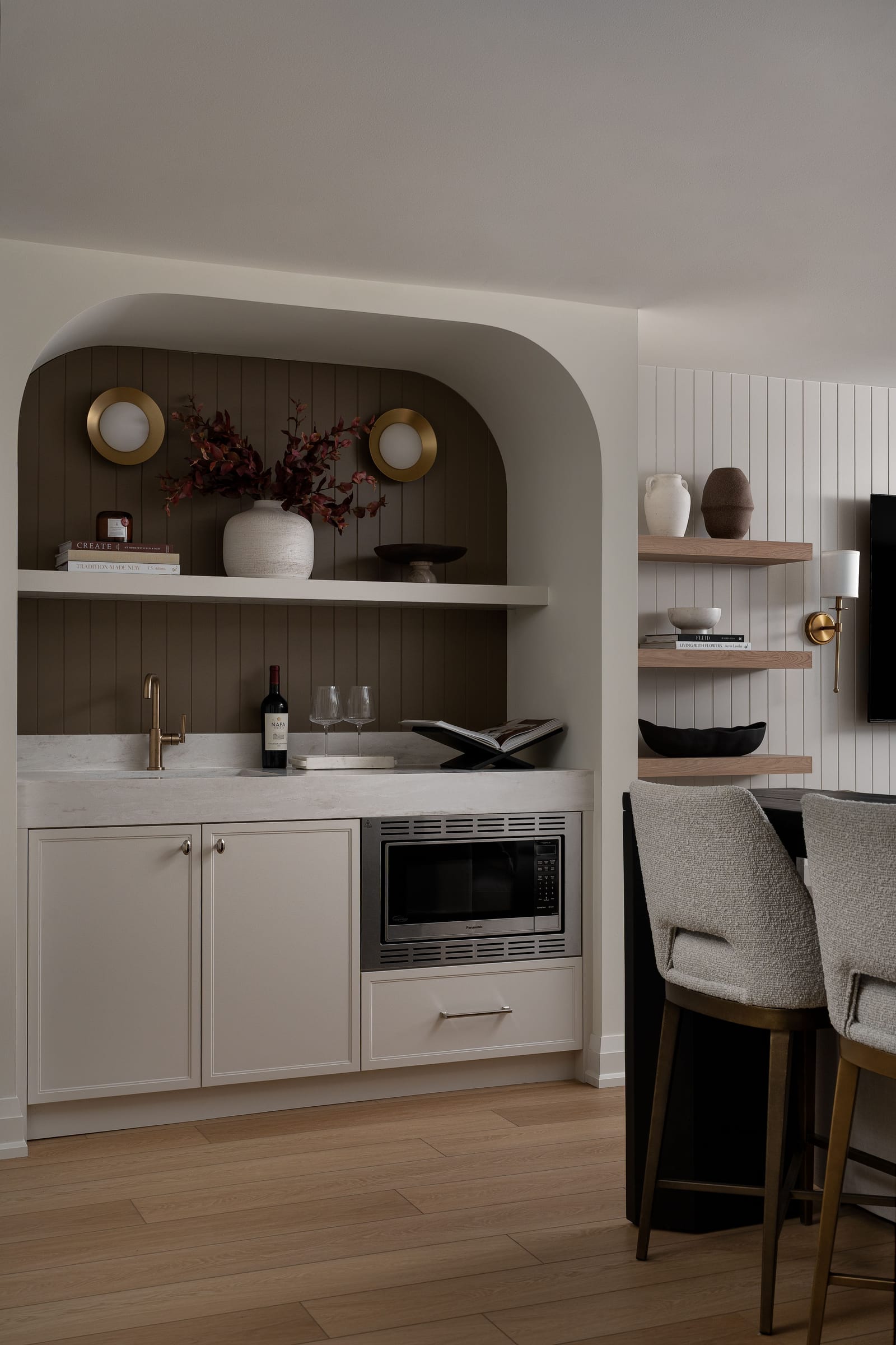 Side view of the arched wet bar and the edge of a dark-based island with two boucle stools on an oak floor